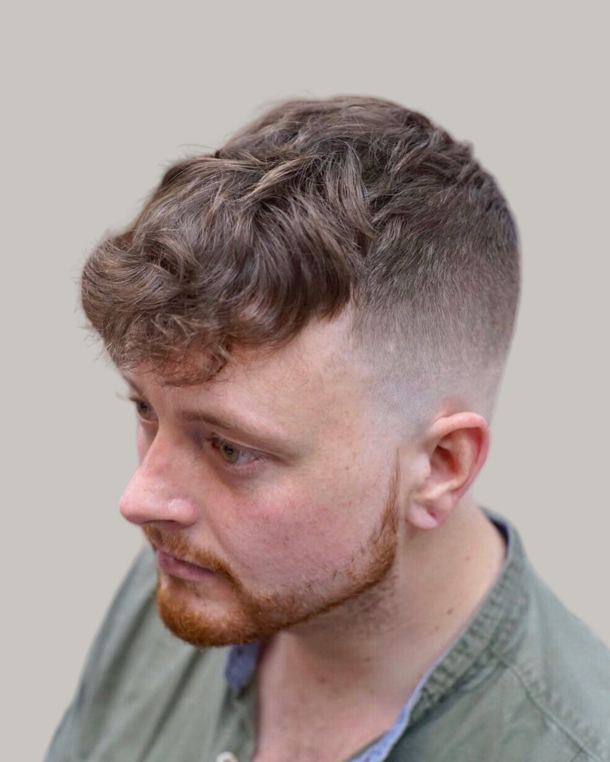 Man with a ginger beard and a wavy textured fringe over a taper fade, looking down to one side