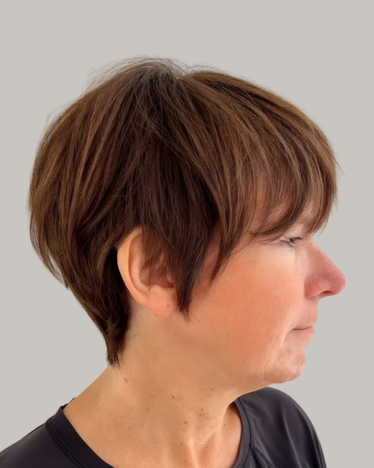 Woman with a short brown pixie bob and a long fringe, seen in profile