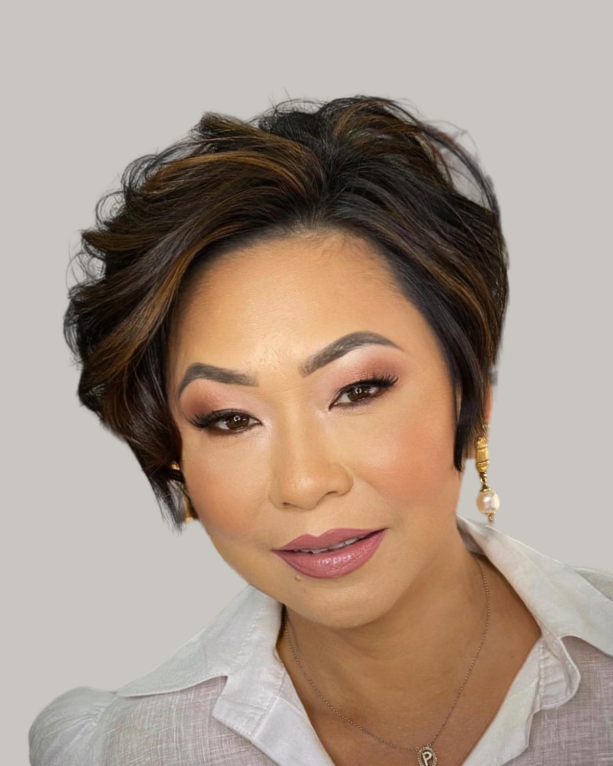 Woman with a dark brown bixie with caramel highlights, facing the camera