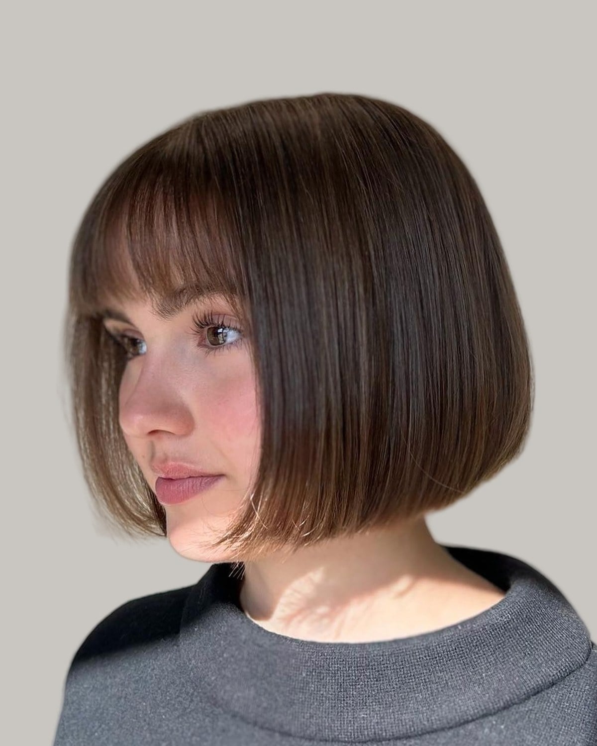 Woman with a brown chin-length bob and straight bangs, in three-quarter view