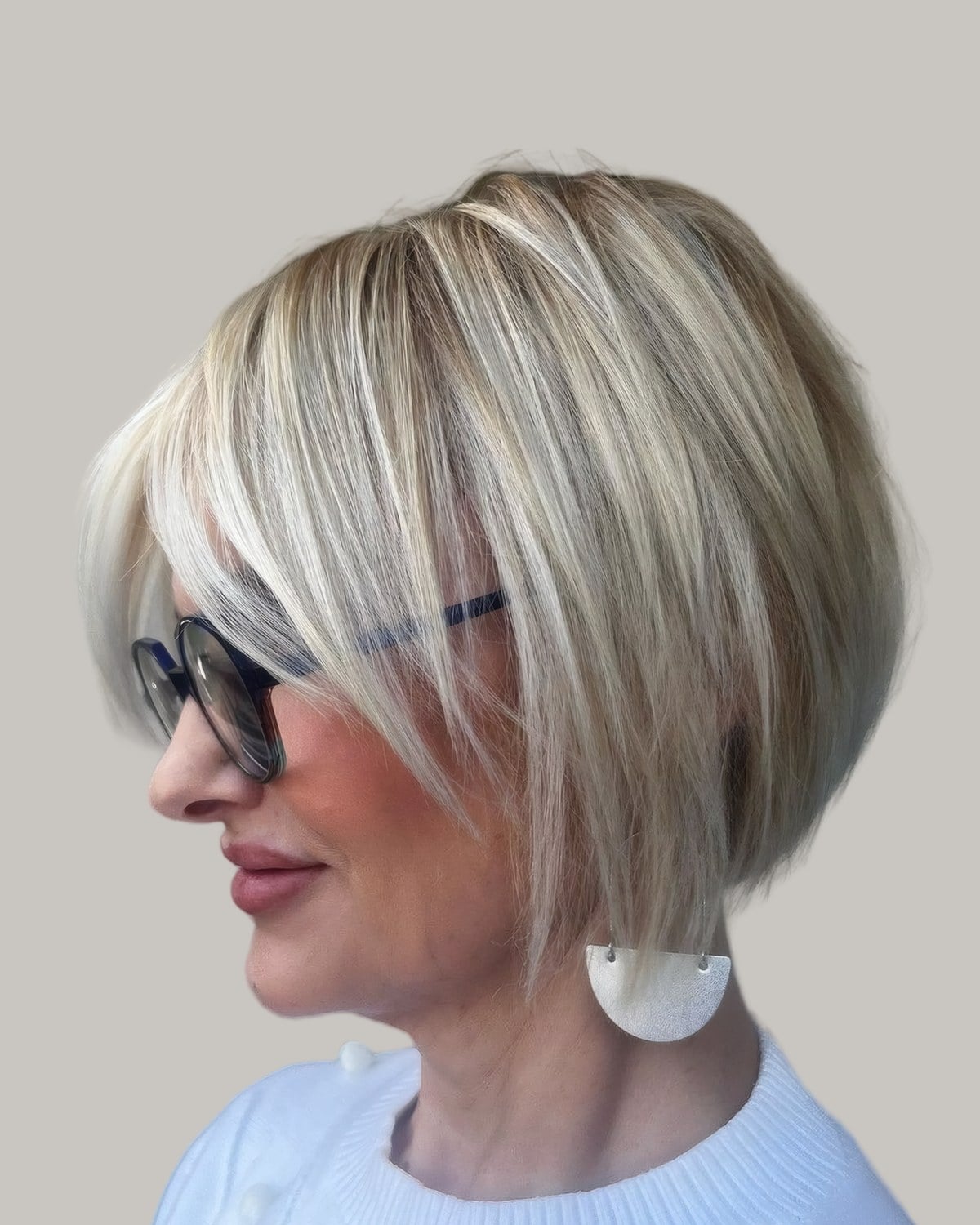 Woman with a blonde bob, long side bangs and dark glasses, seen in profile