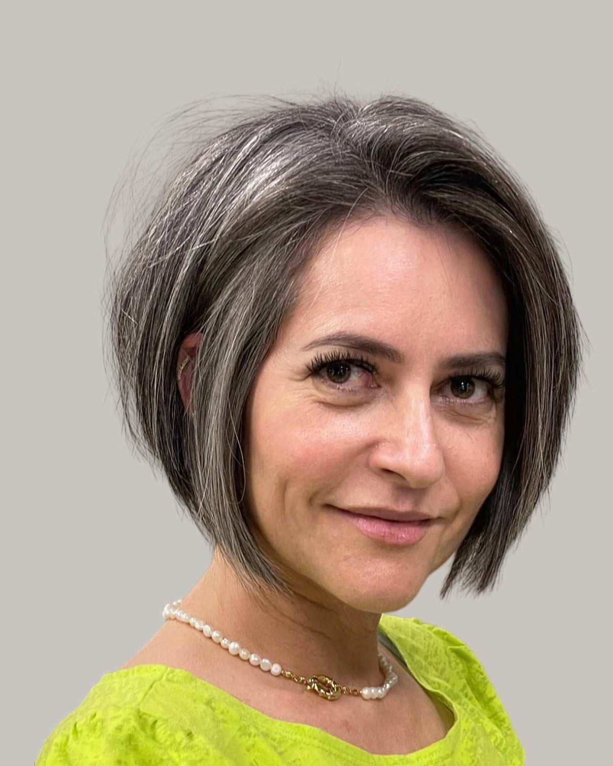 Smiling woman with a gray and brown bob and a deep side part, facing the camera