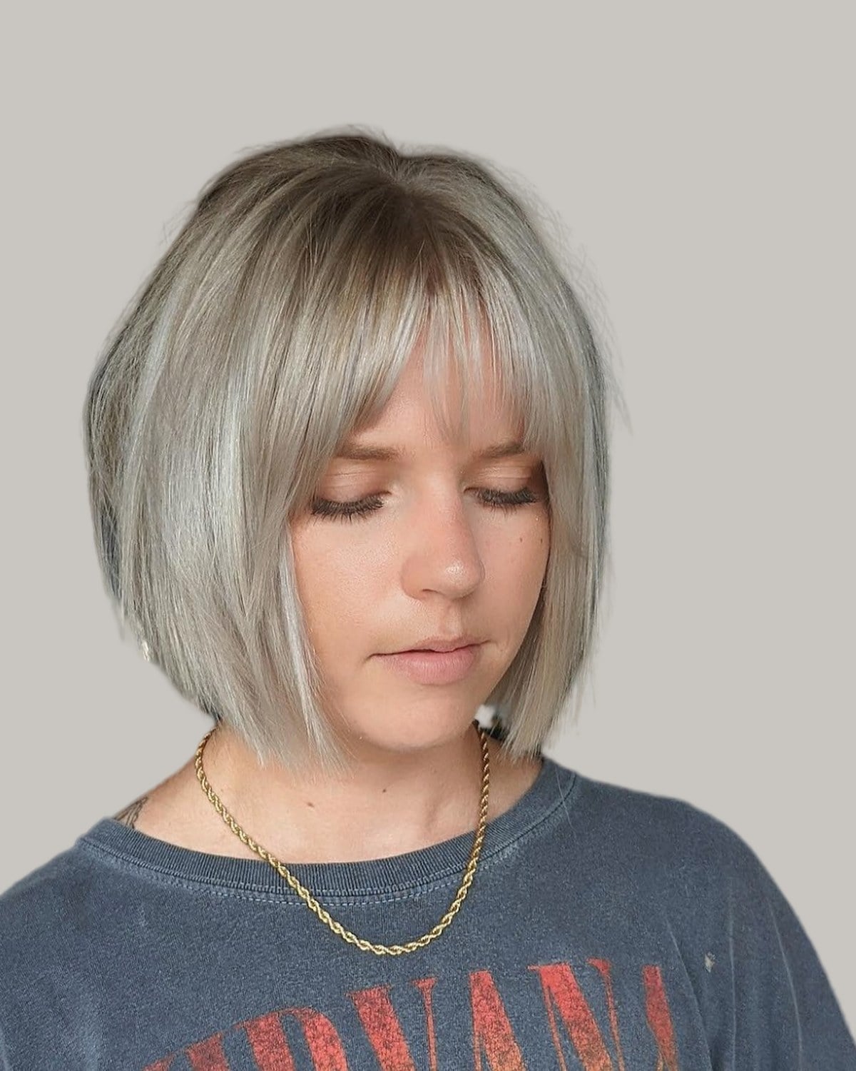 Woman with an ash-blonde chin-length bob and wispy bangs, looking down