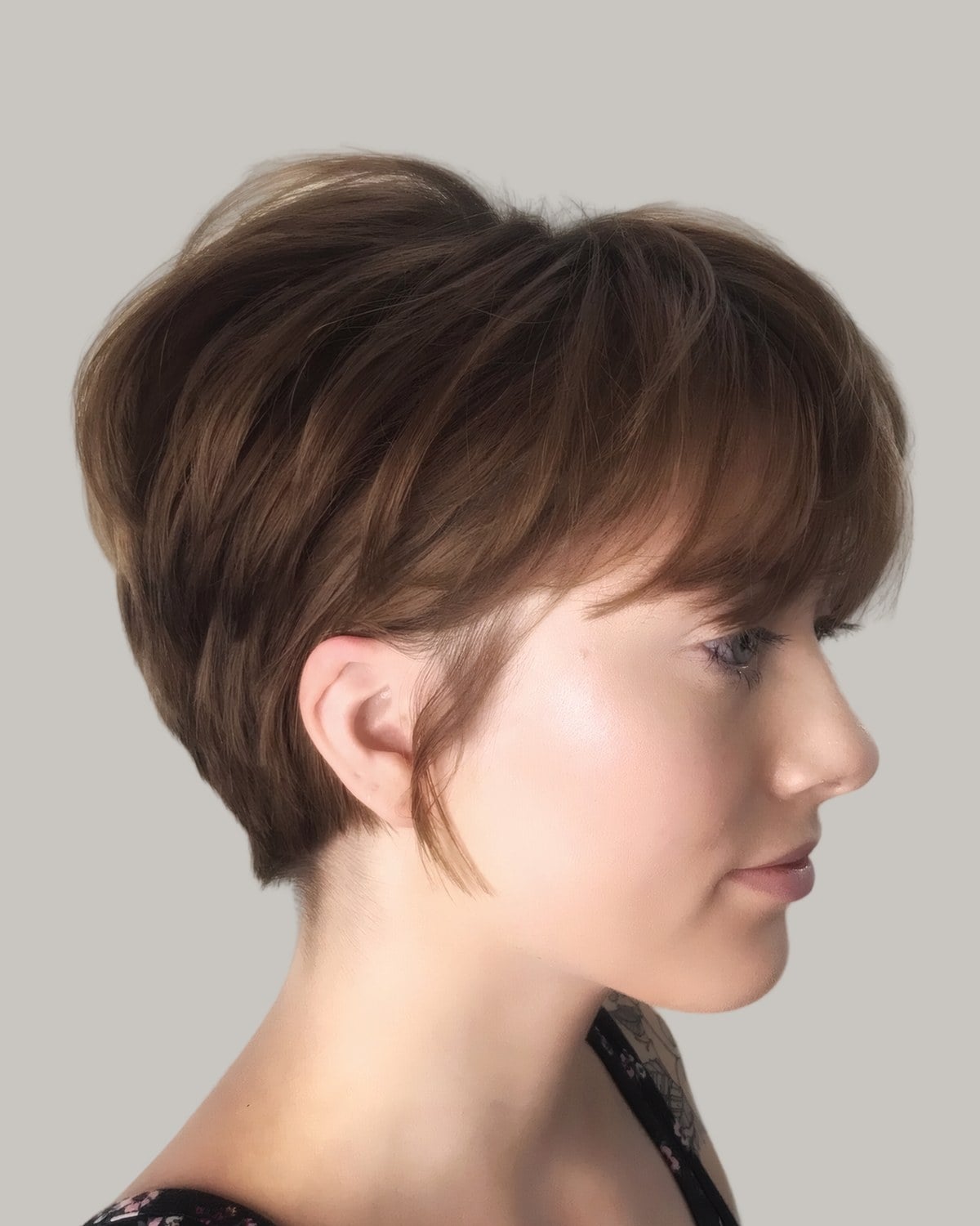 Woman with a brown pixie bob and a long side fringe, seen in profile
