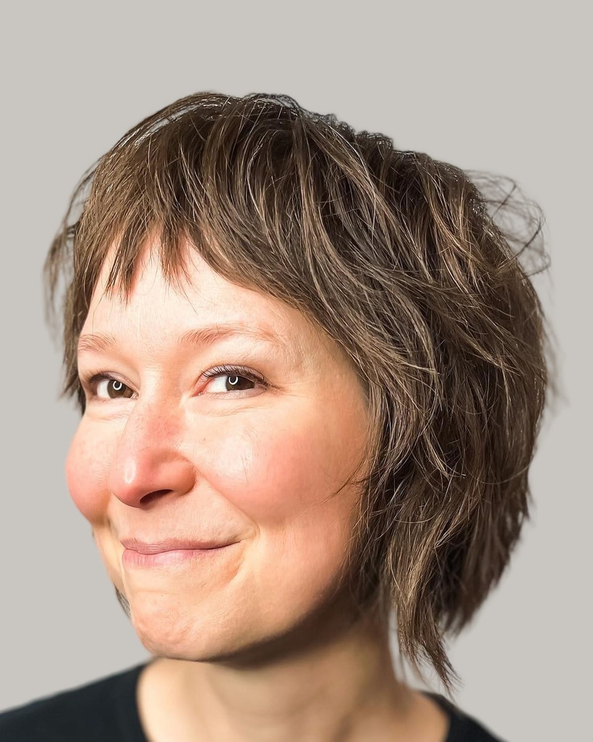 Smiling woman with a brown shaggy bob and short bangs, facing the camera
