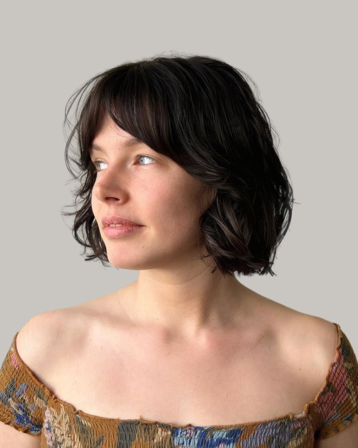 Woman with a dark wavy bob and bangs, in three-quarter view