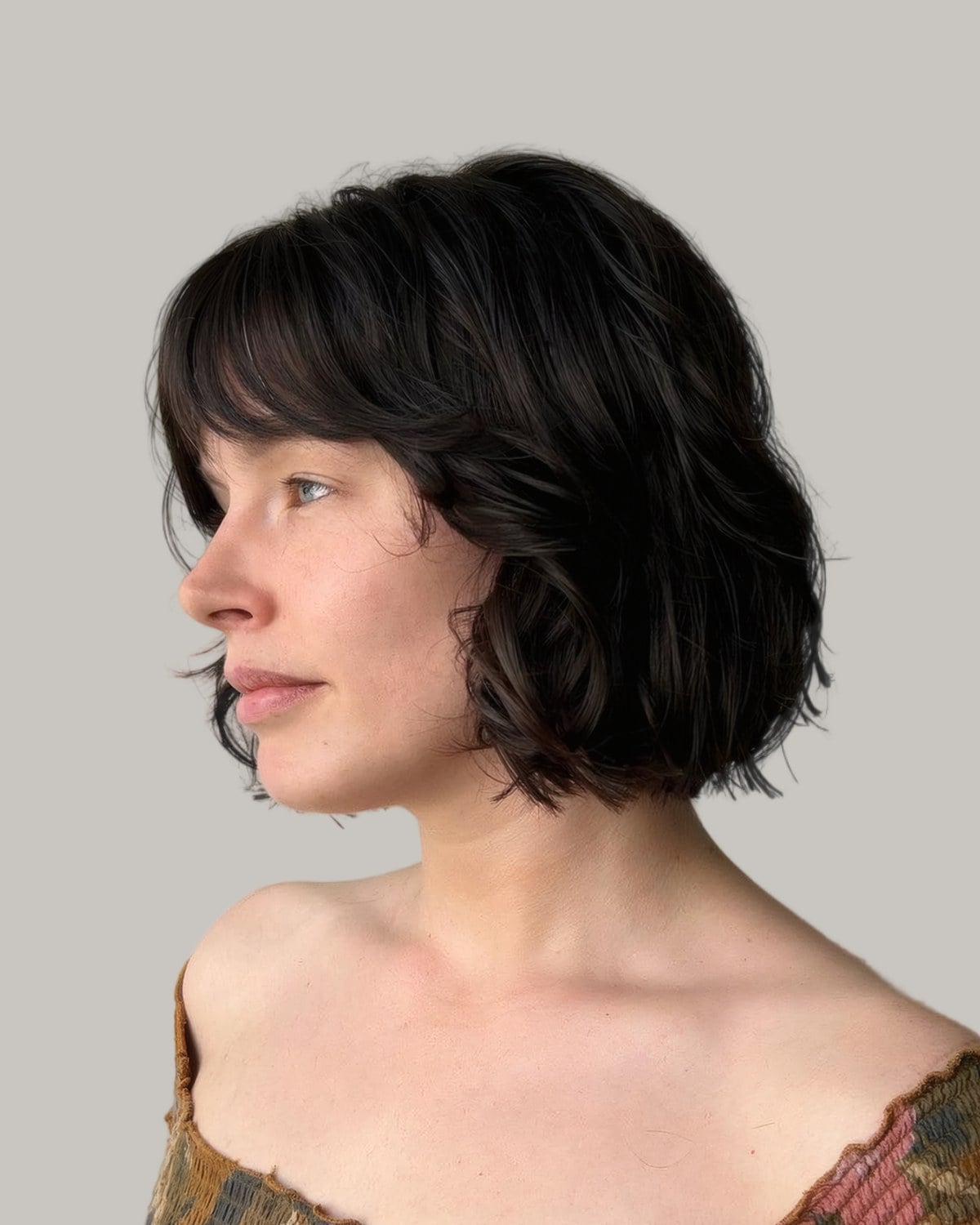Woman with a dark wavy bob and bangs, seen in profile
