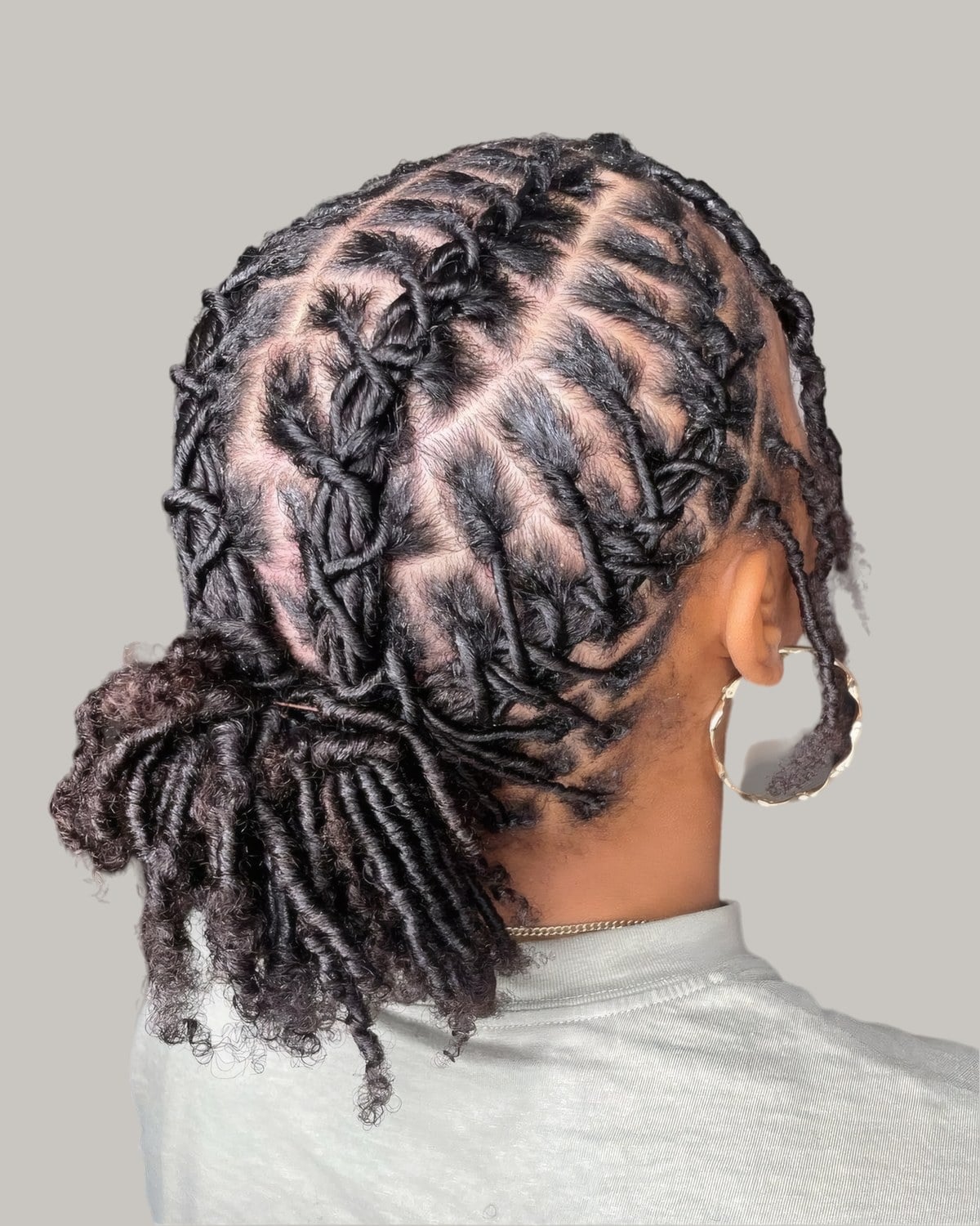 Woman with locs gathered into a low bun, parts crossing at the back