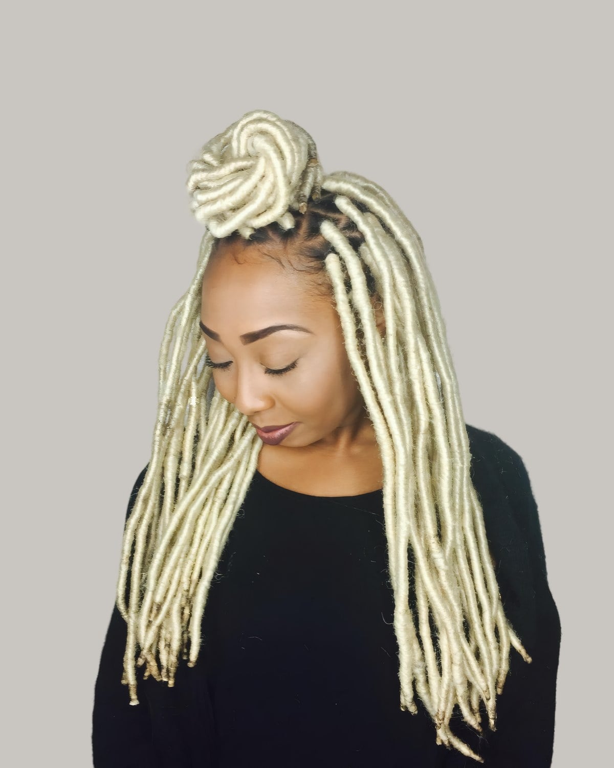 Woman with platinum faux locs, the top in a high bun, looking down