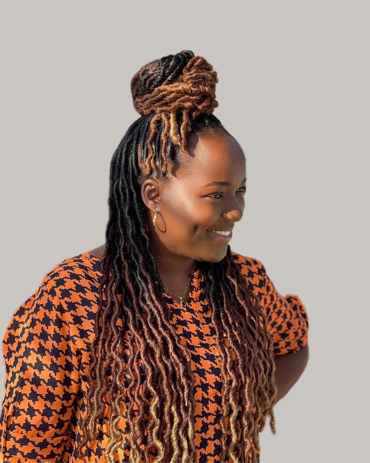 Smiling woman with honey-brown locs half up in a bun