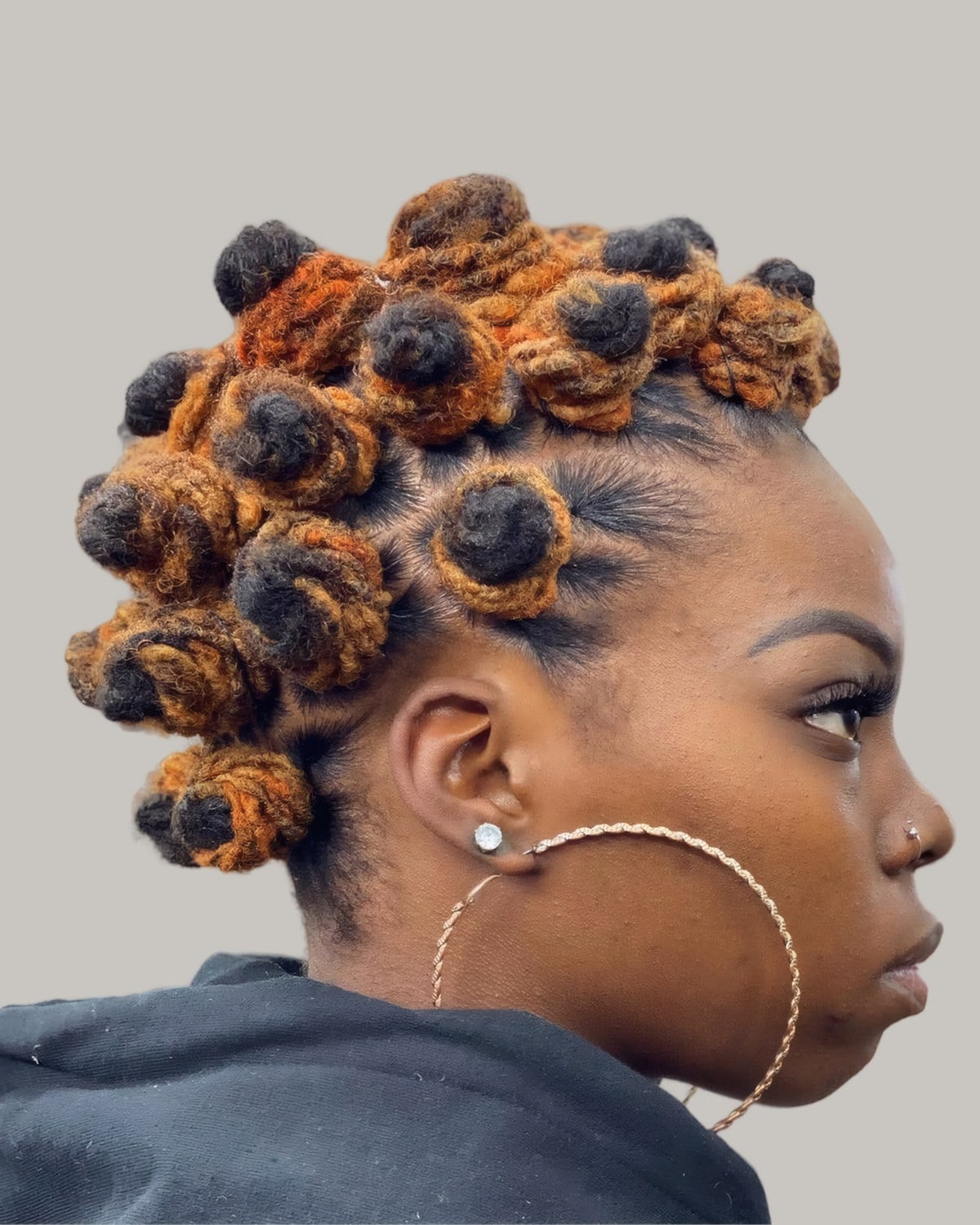 Woman with honey and brown locs twisted into many small Bantu knots, in profile