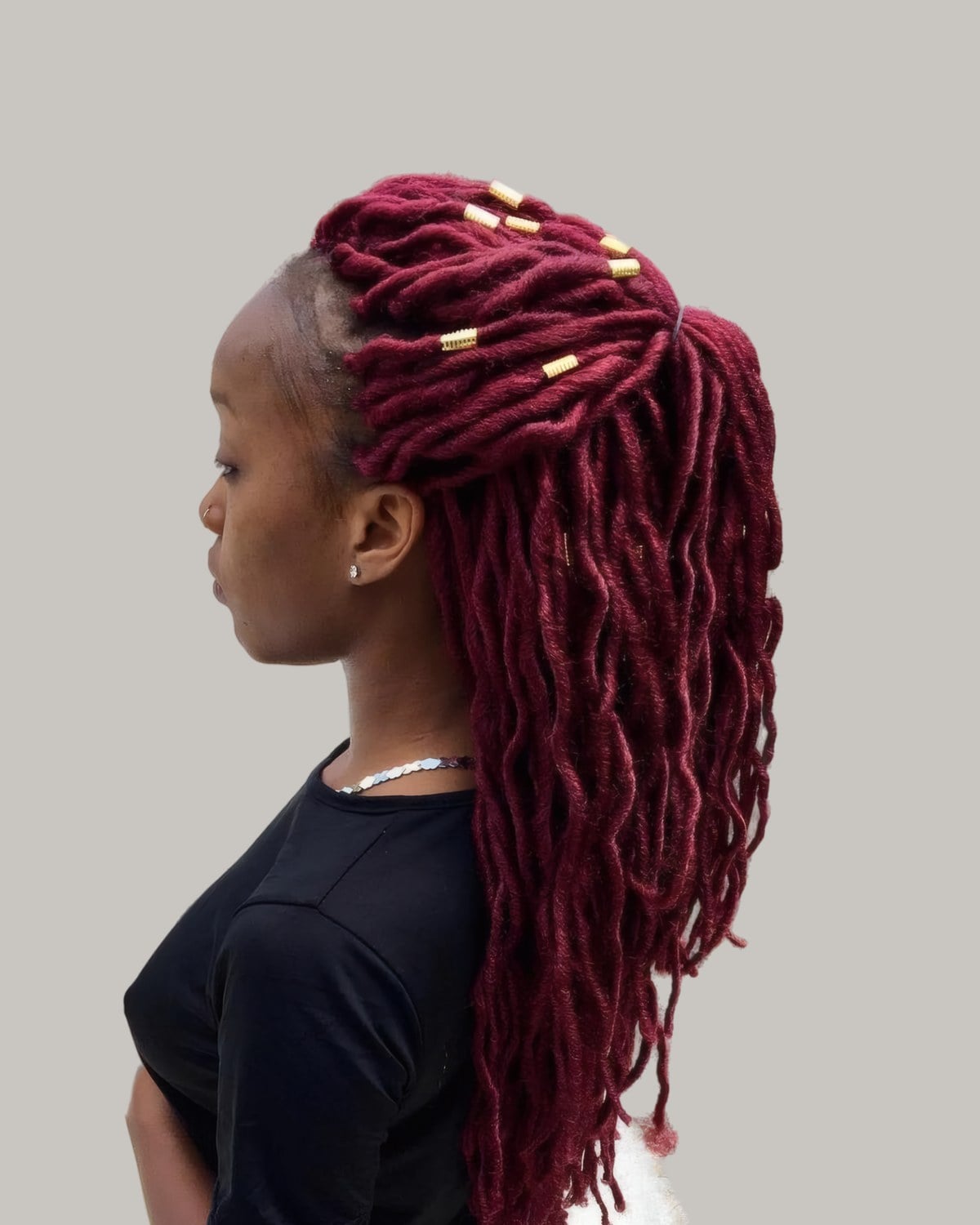 Woman with burgundy locs gathered at the crown with gold cuffs, in profile