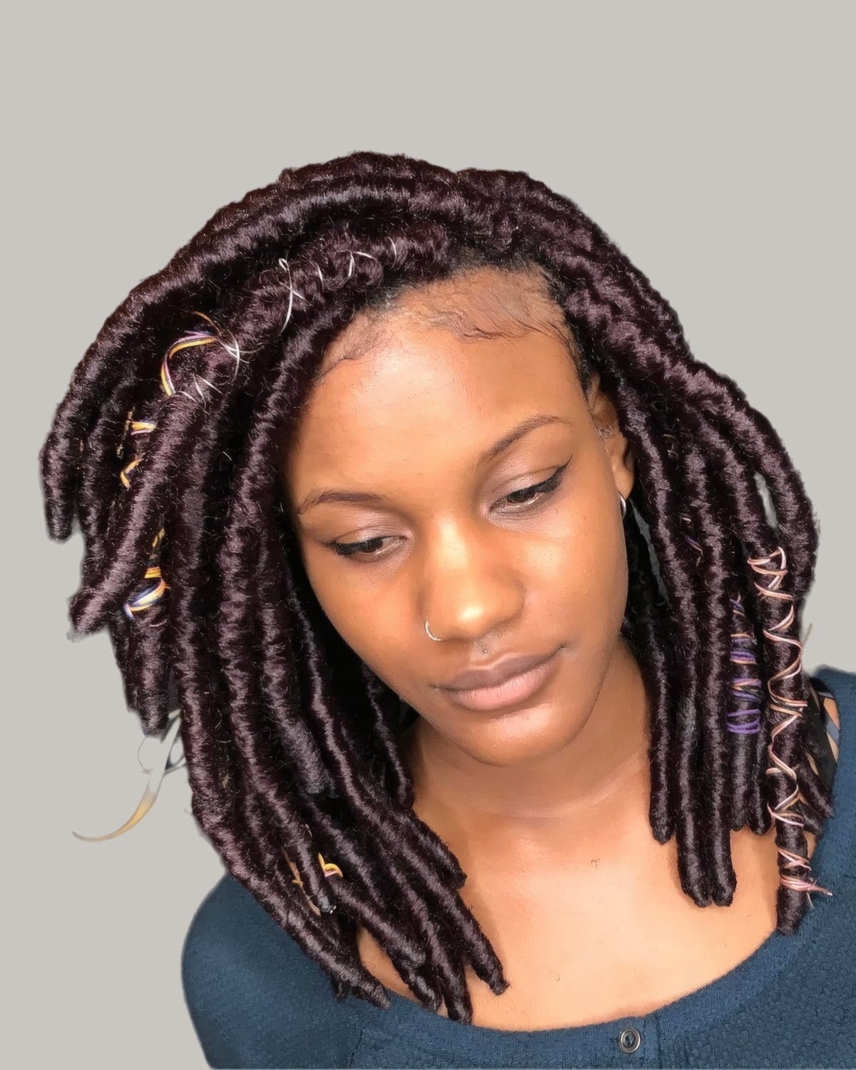 Woman with shoulder-length black and burgundy faux locs, looking down