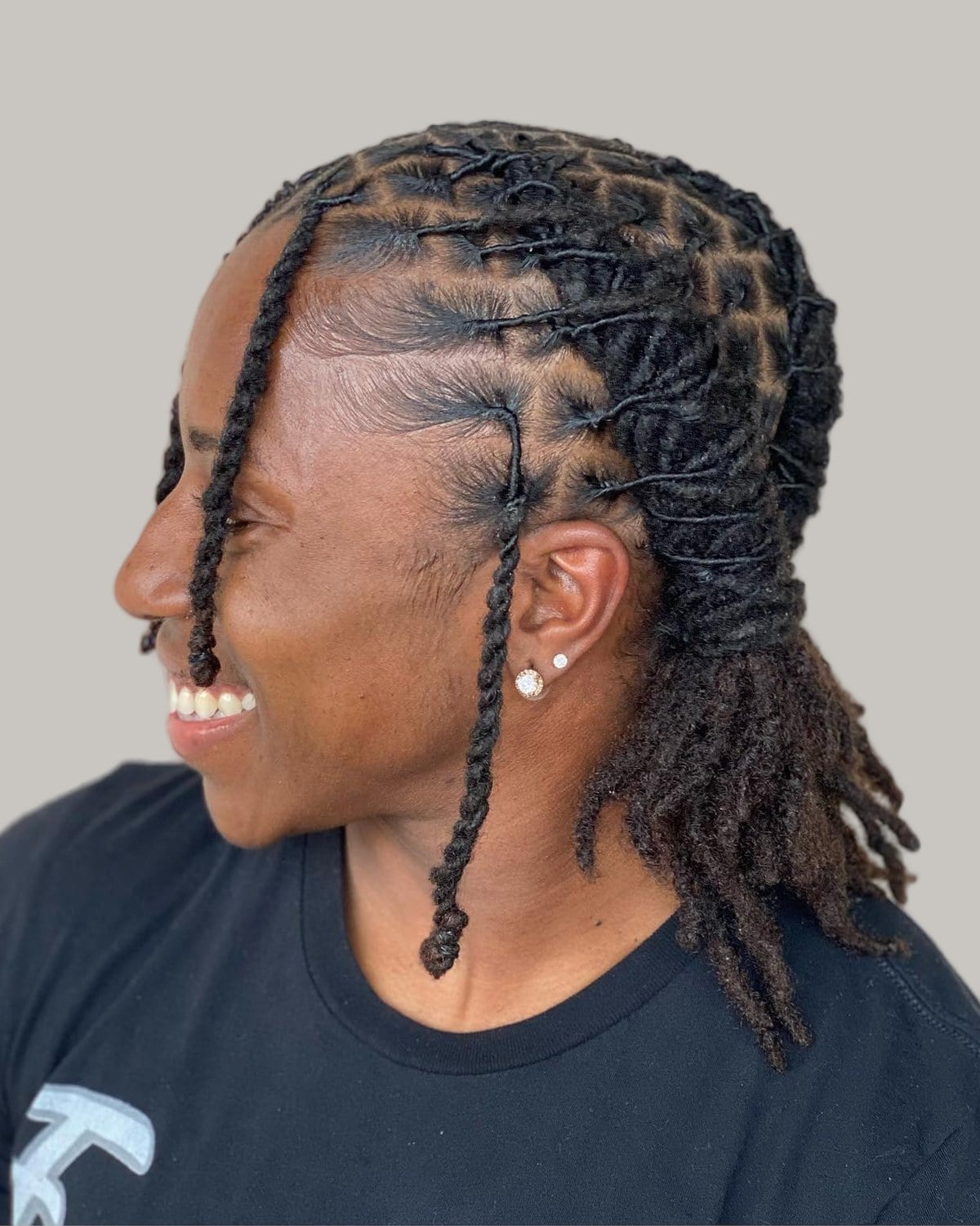 Smiling woman with front locs twisted back and the rest hanging, in profile