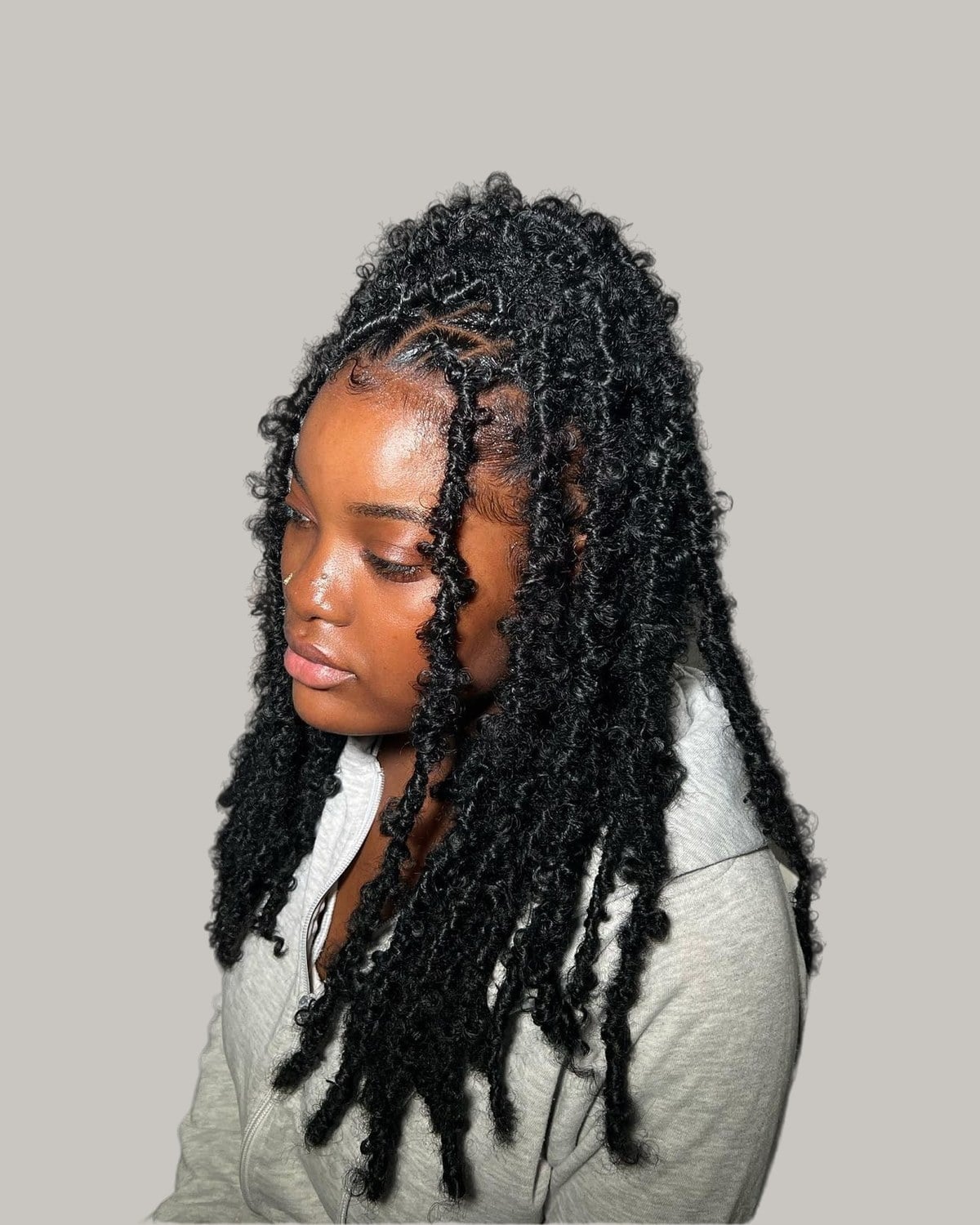 Woman with long black locs, the top section up, looking down