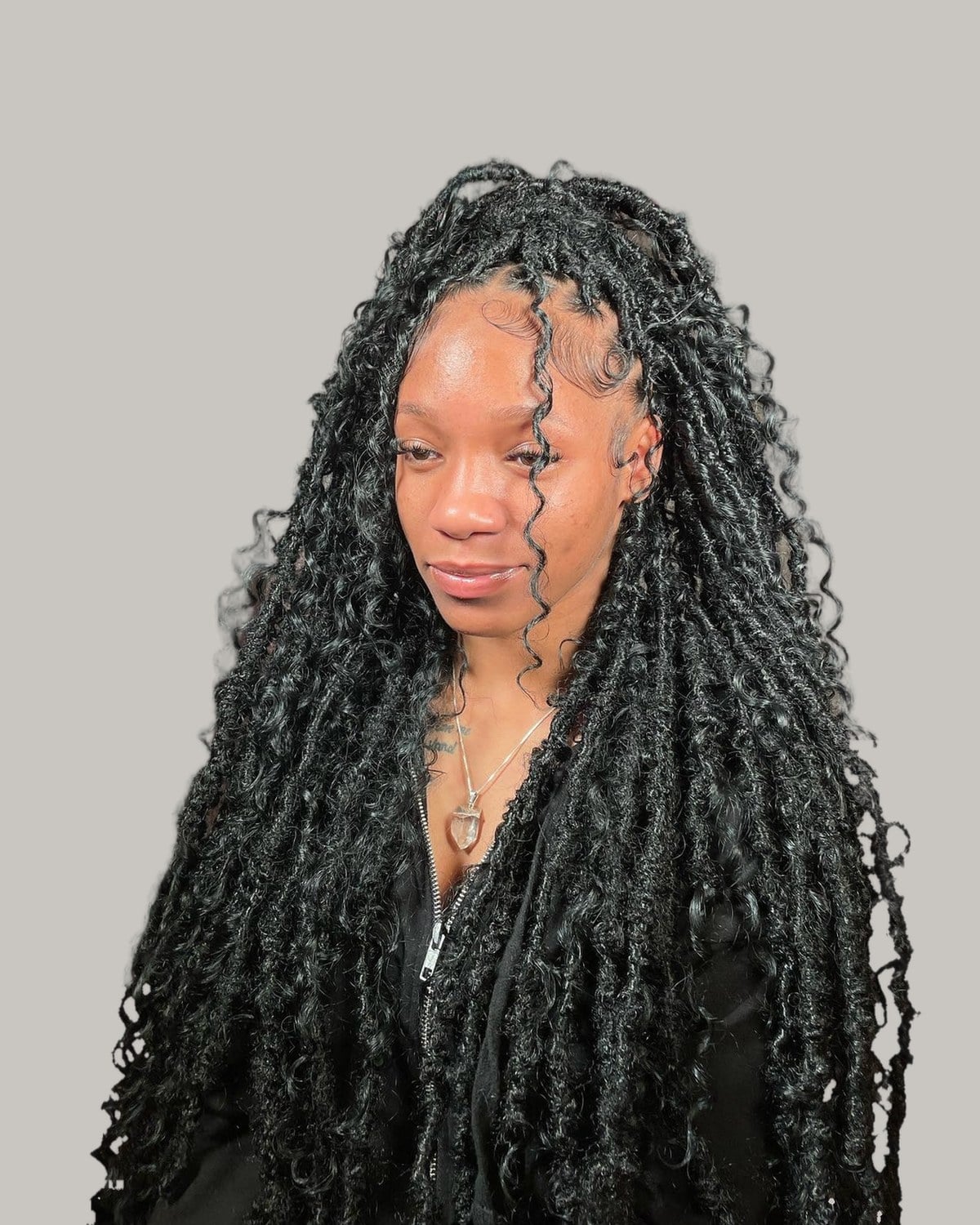 Woman with long black butterfly locs with curly pieces, swept over one shoulder