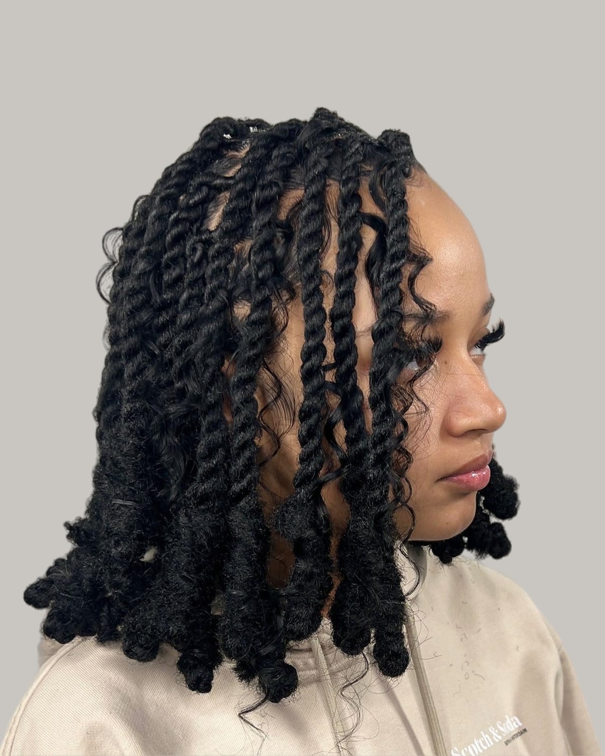 Woman with a black twisted loc bob with curled ends, in profile