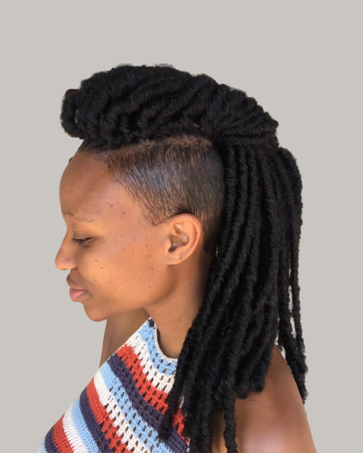 Woman with long black locs over a shaved side, in profile