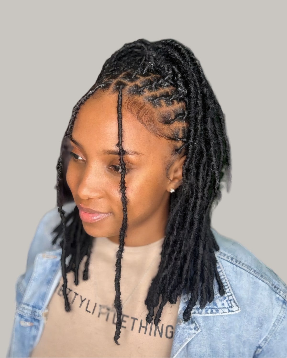 Woman with locs pulled back into a ponytail, a few left down at the front