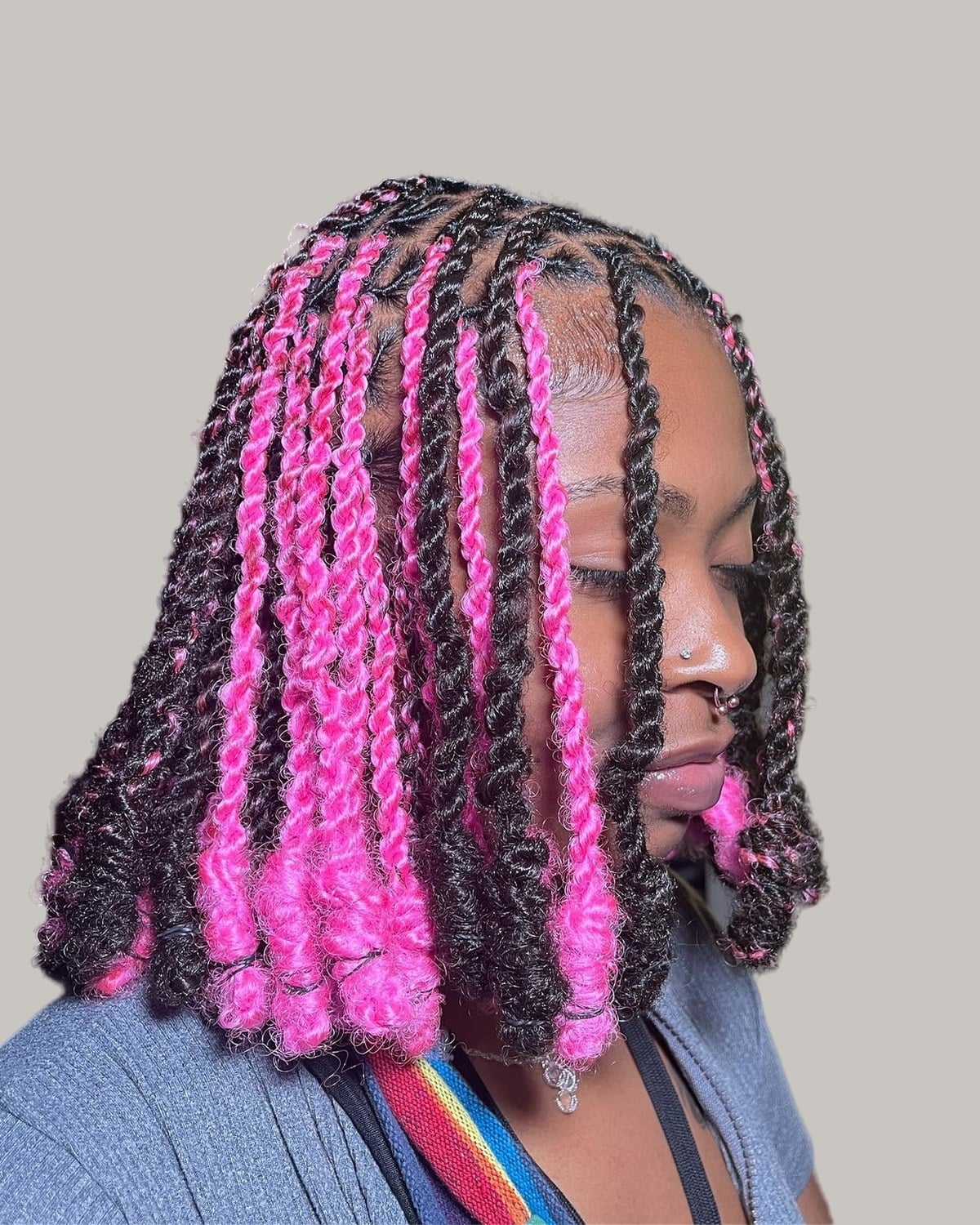 Woman with dark twists and bright pink strands, looking down