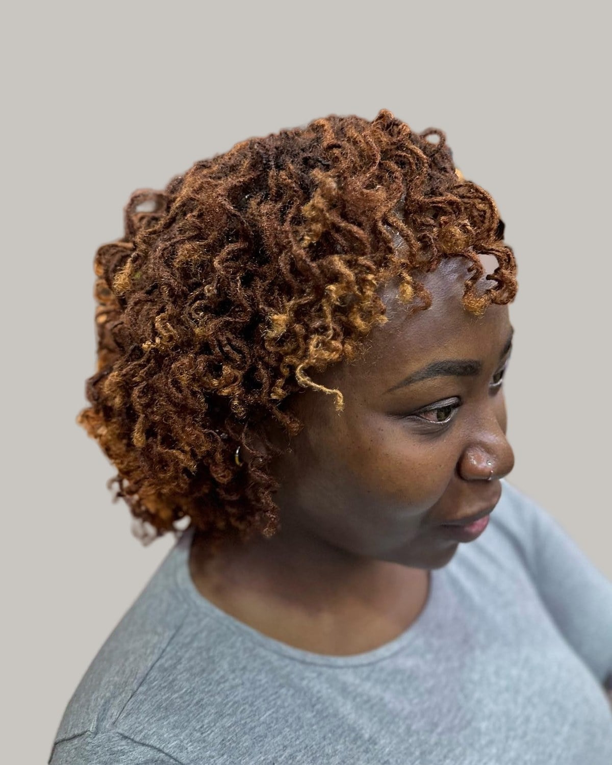 Woman with short copper-brown locs curled toward her face, looking down