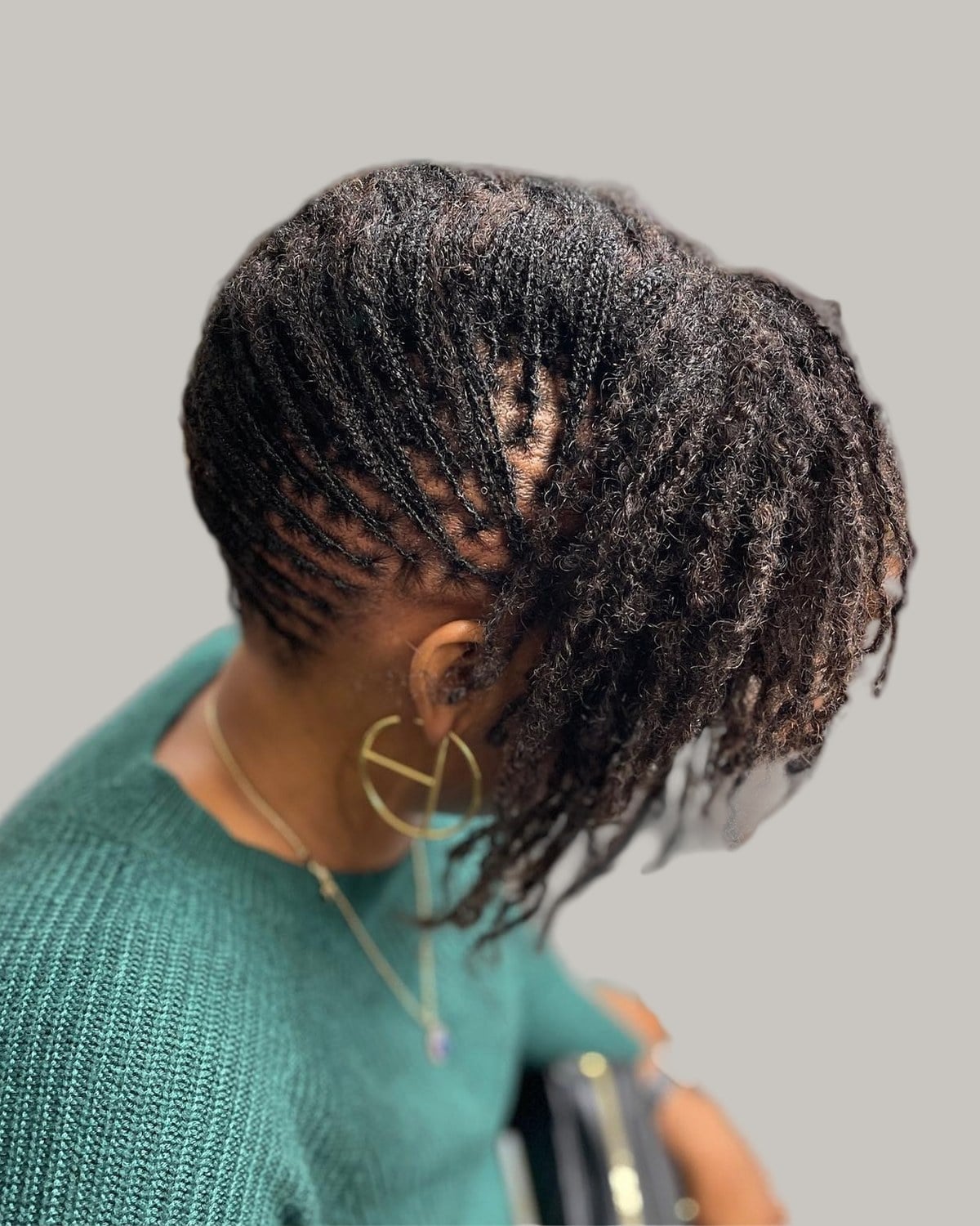 Woman with short black locs swept to one side, looking down