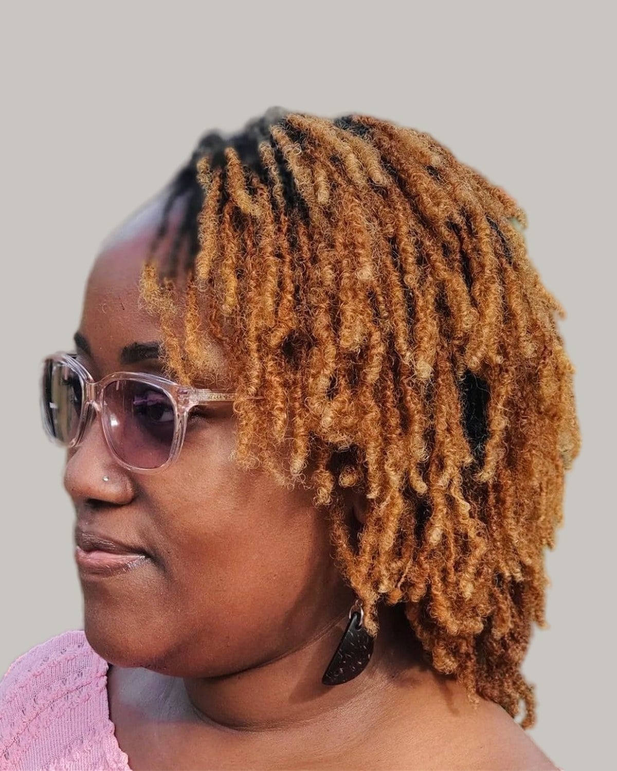 Woman with copper curly locs swept to one side and pink glasses