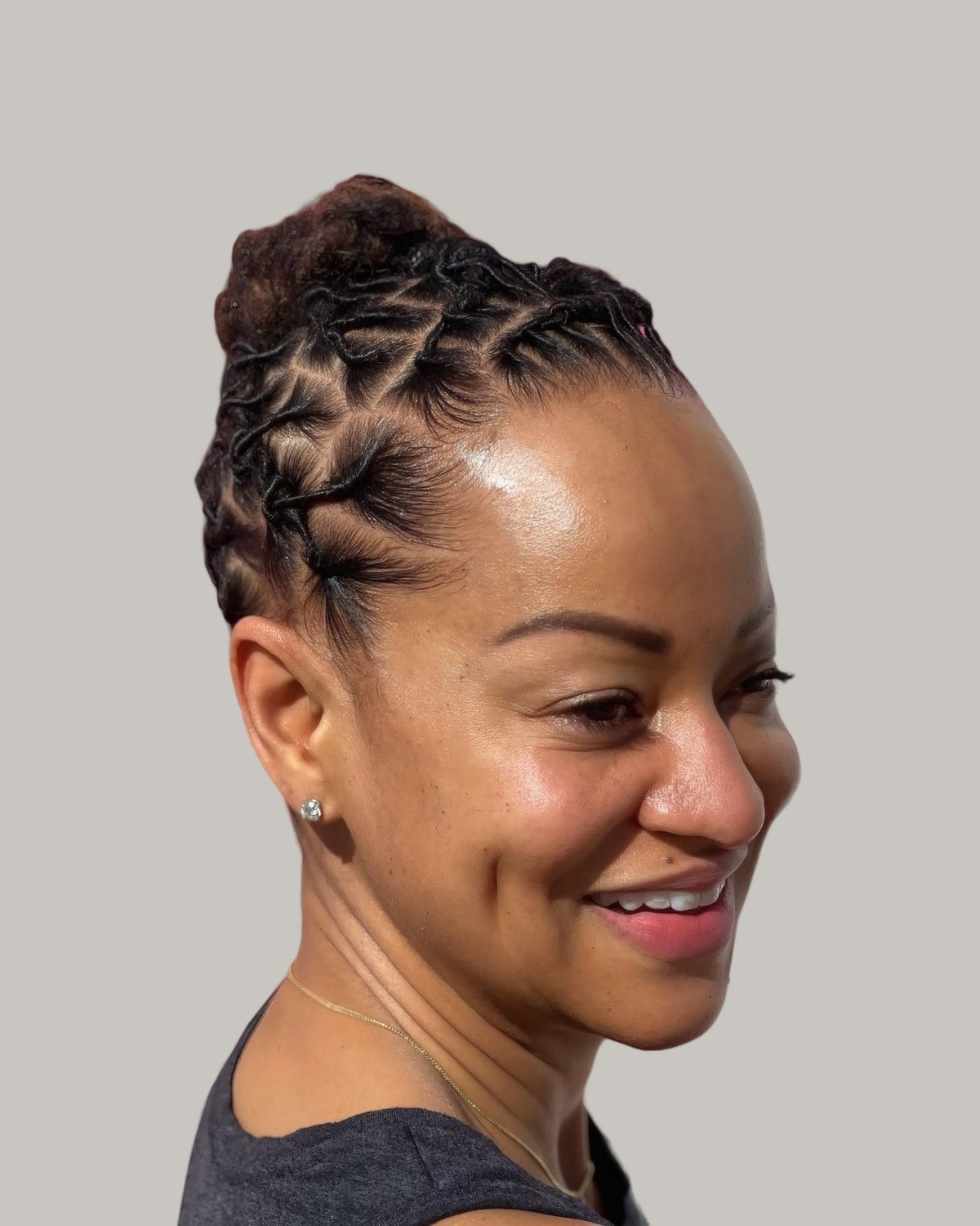 Smiling woman with short locs twisted up into a small bun, in profile