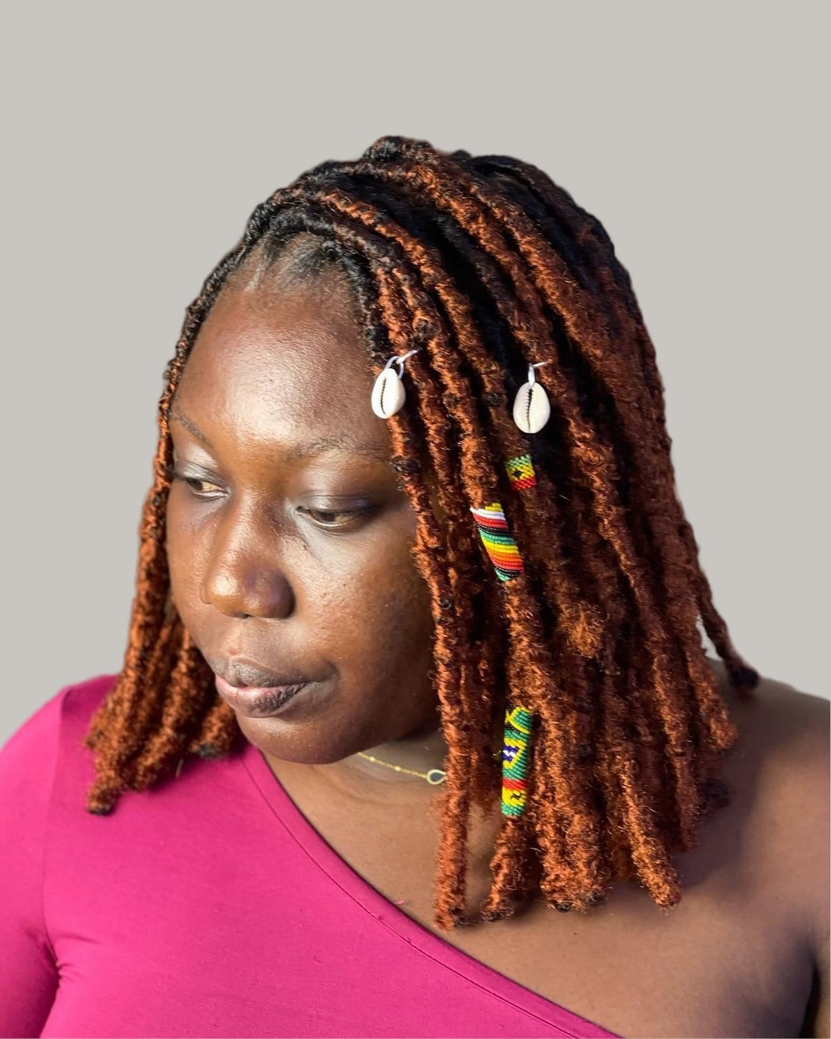 Woman with copper locs, cowrie shells and colored thread wraps, looking down