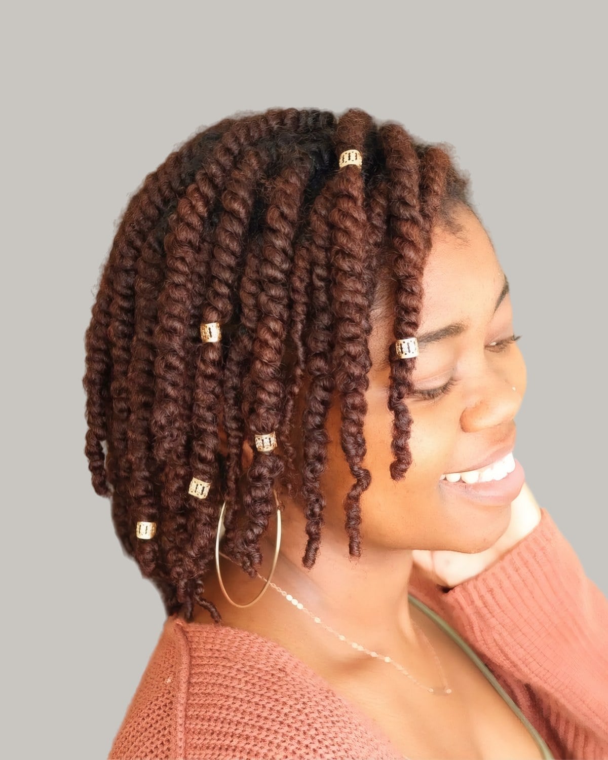 Smiling woman with copper two-strand locs and gold cuffs