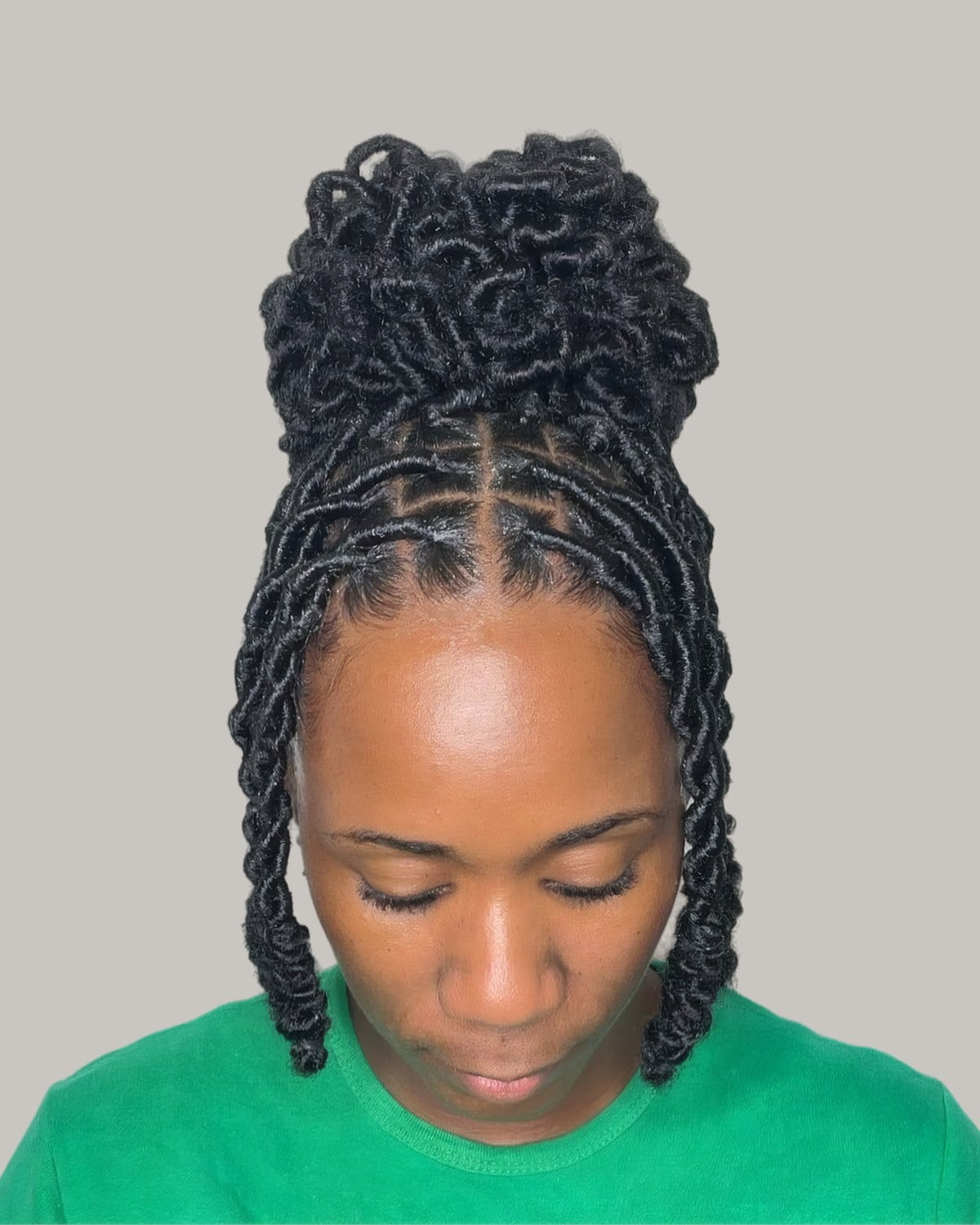 Woman with crochet locs piled into a curly bun, a few down at the sides, looking down