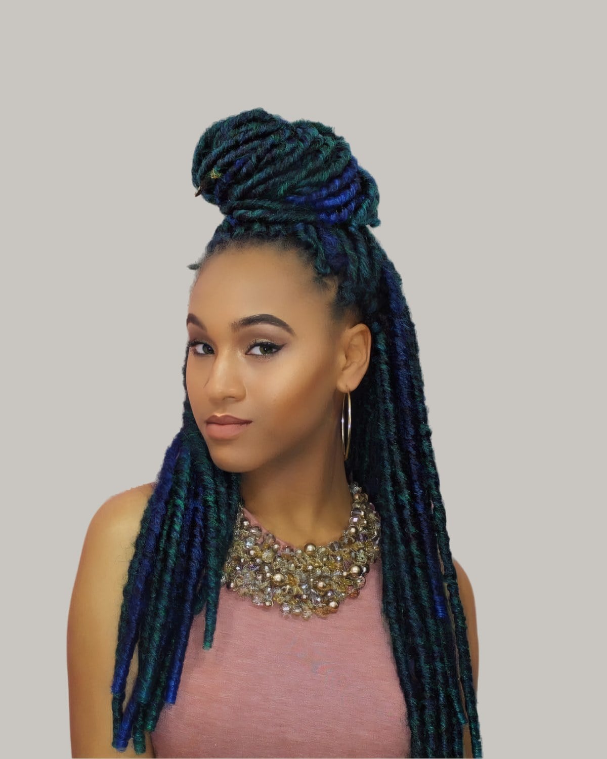 Woman with teal and black locs, the top in a high bun and the rest down