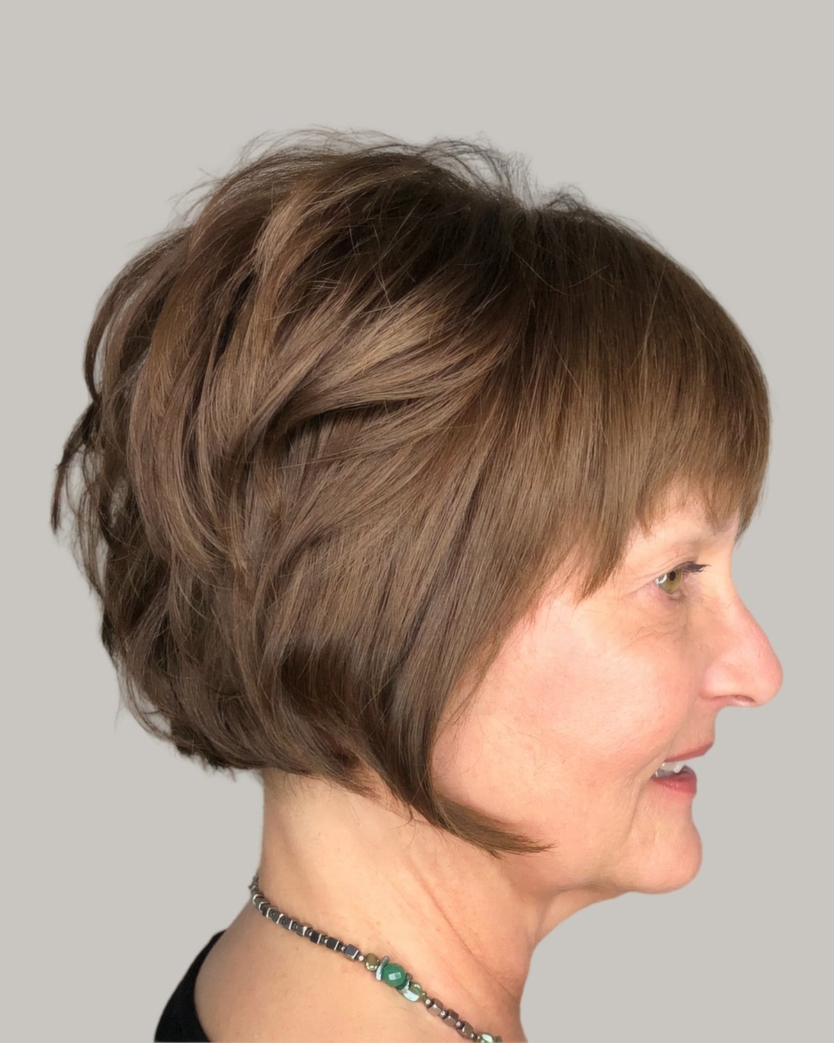 Smiling woman with a light-brown stacked bob and a fringe, seen in profile