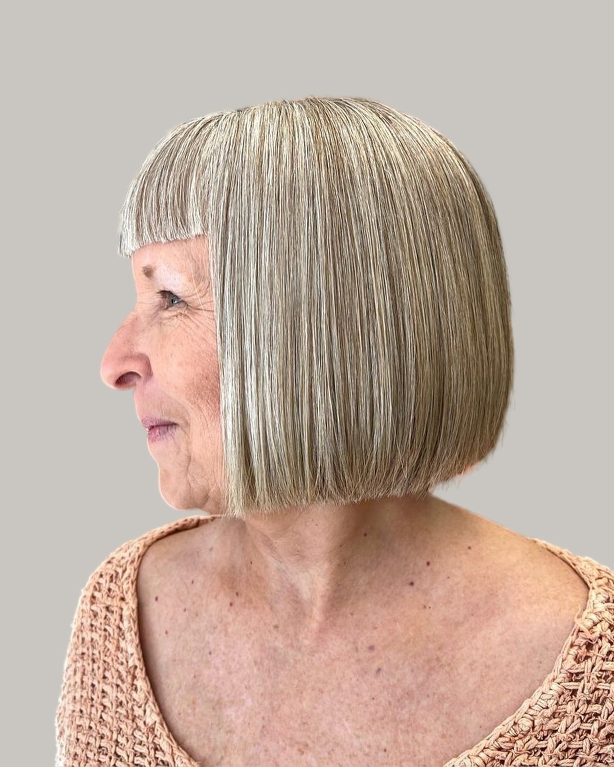 Woman with a silver blunt bob and short baby bangs, seen in profile