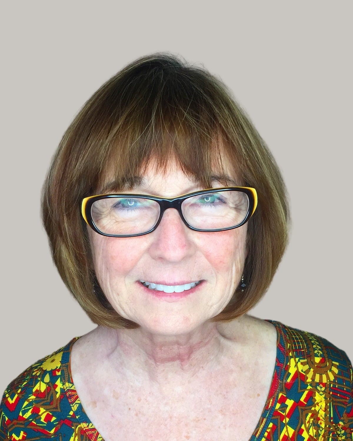 Smiling woman with a brown bob, a full fringe and black glasses