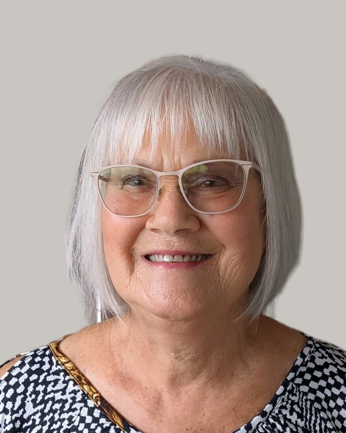 Smiling woman with a white bob, a full fringe and clear glasses