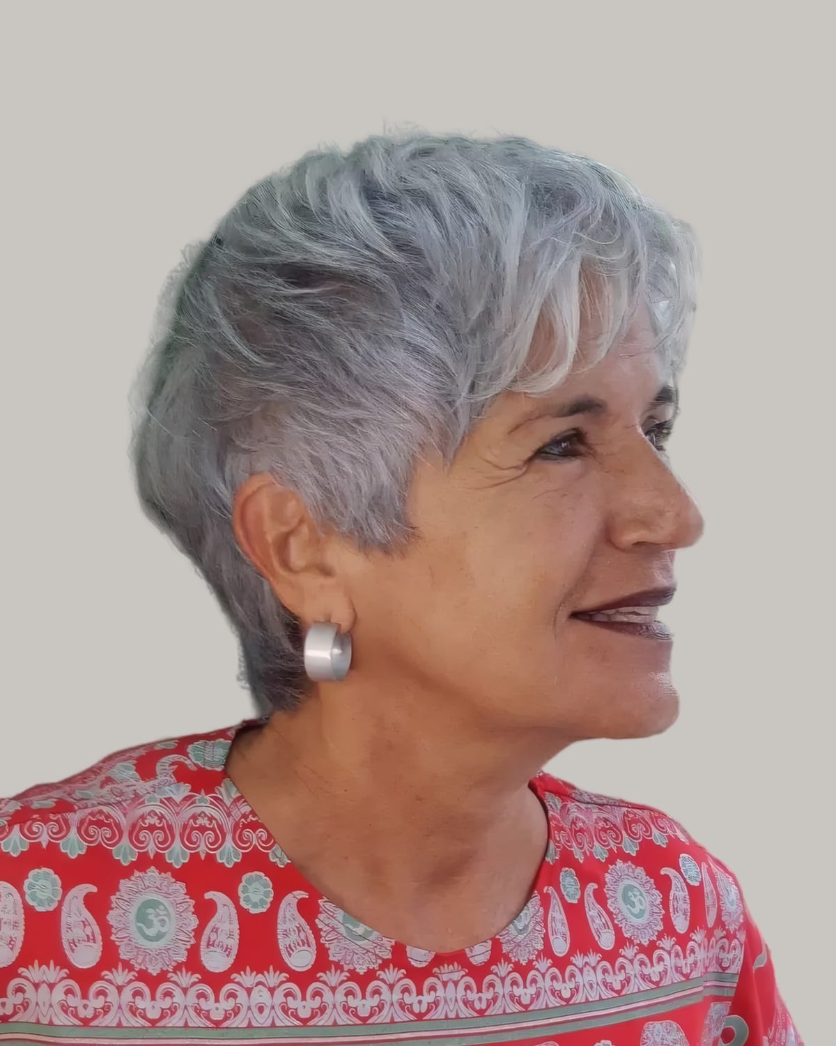 Smiling woman with a short silver pixie and layered bangs, seen in profile