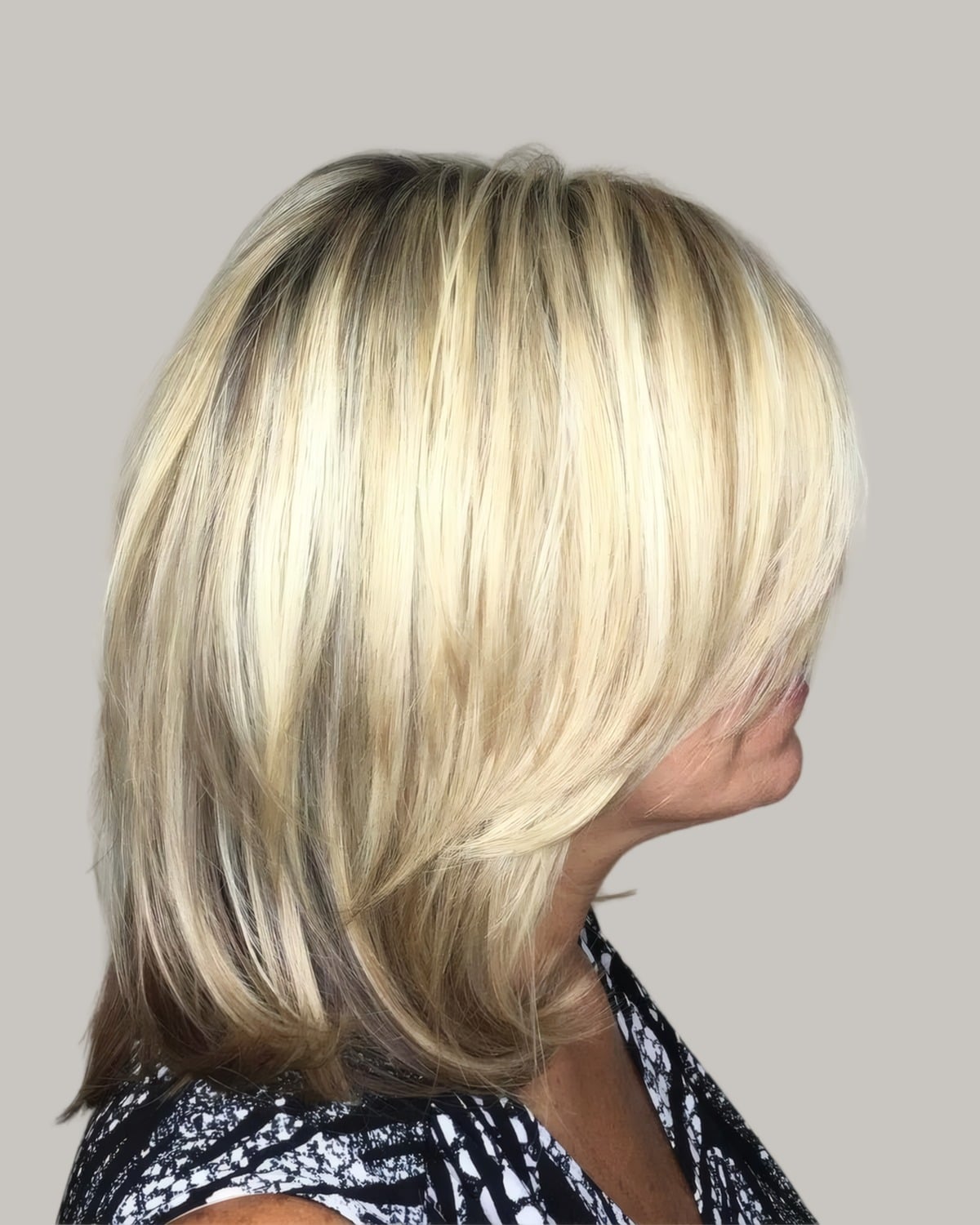 Woman with a blonde layered cut past the shoulders, seen from the side