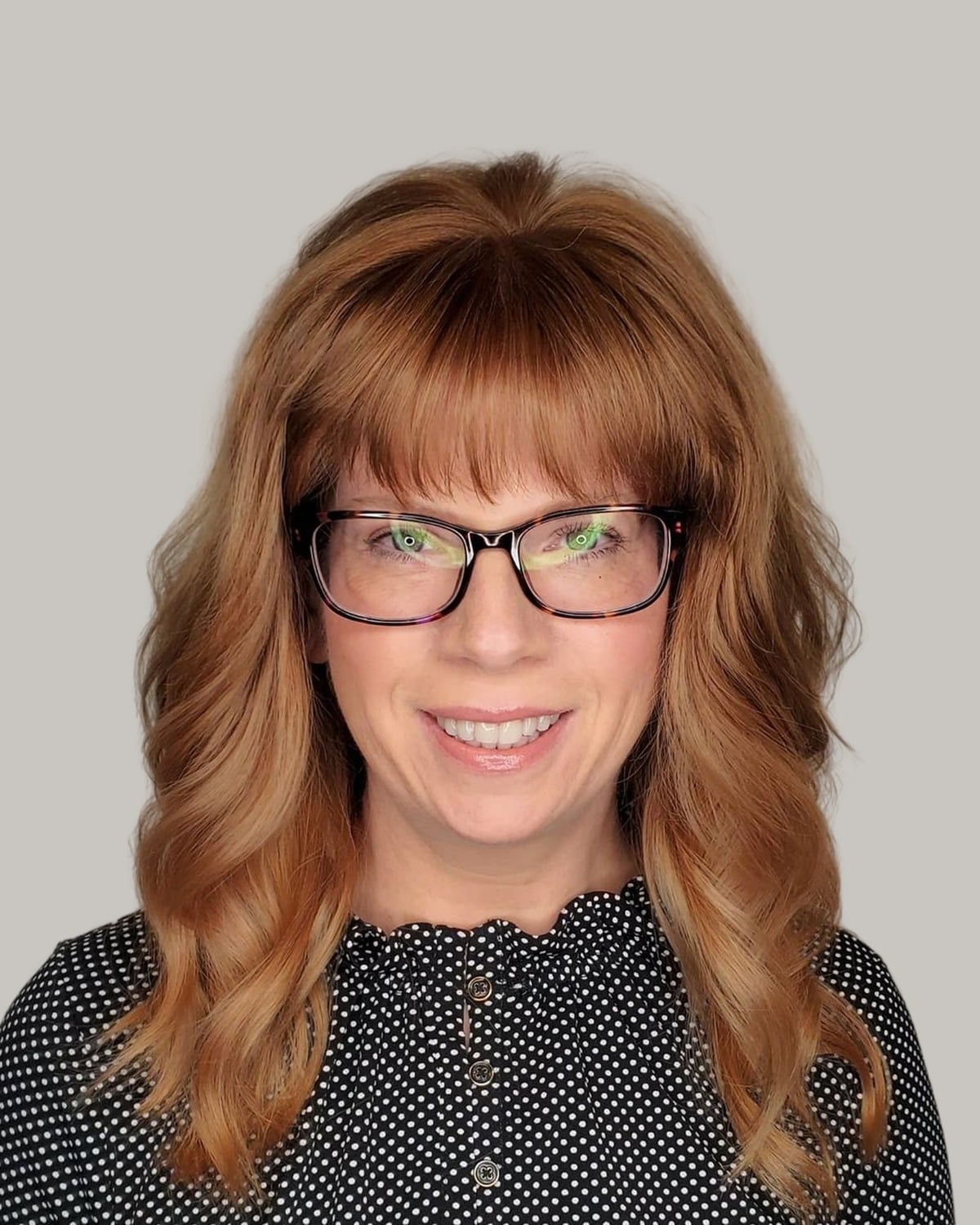 Smiling woman with long copper waves, a full fringe and black glasses