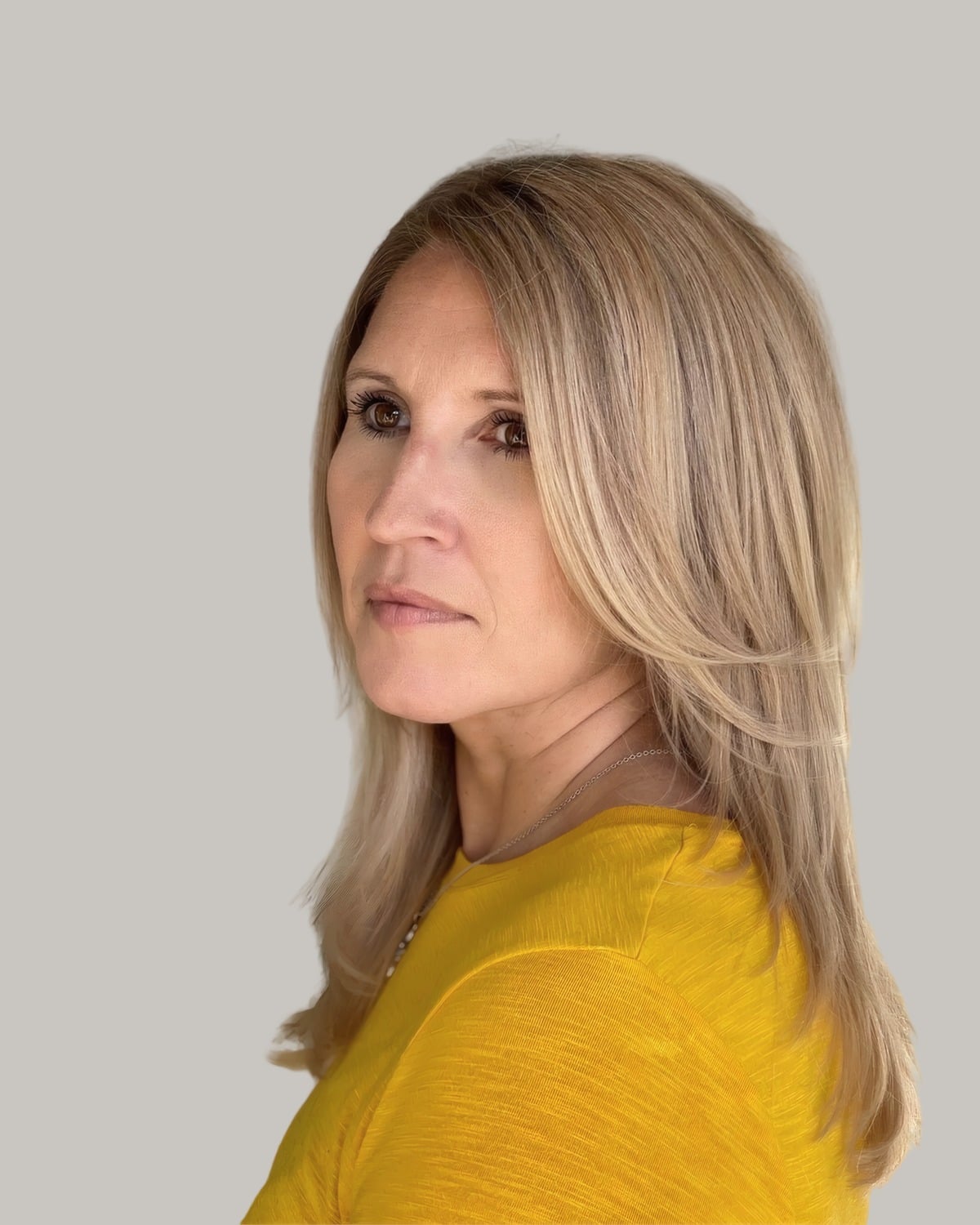 Woman with long blonde layers past the shoulders, in a yellow top