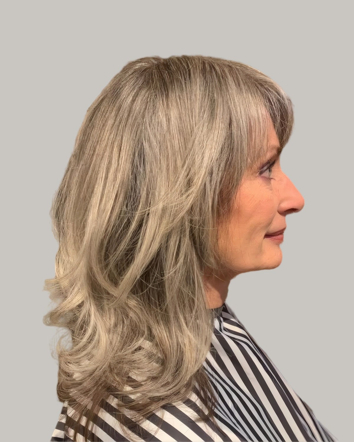 Woman with long ash-blonde layers and side bangs, seen in profile