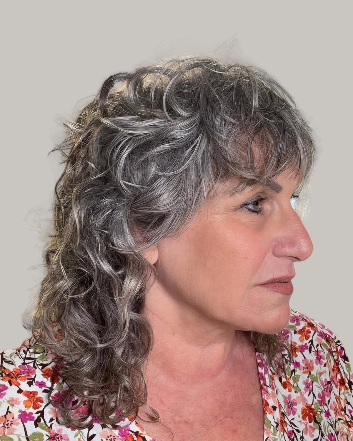 Woman with long salt-and-pepper curls and a curly fringe, seen in profile