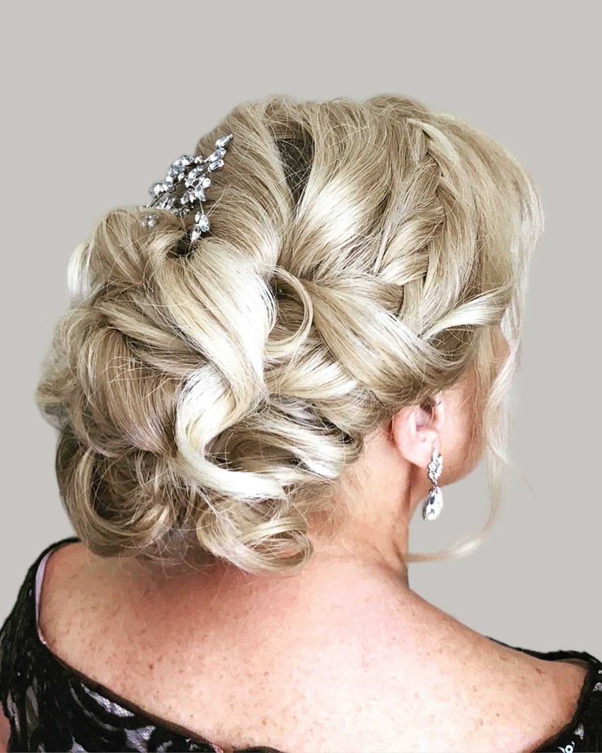 Blonde updo with soft twisted curls and a jeweled pin, seen from behind