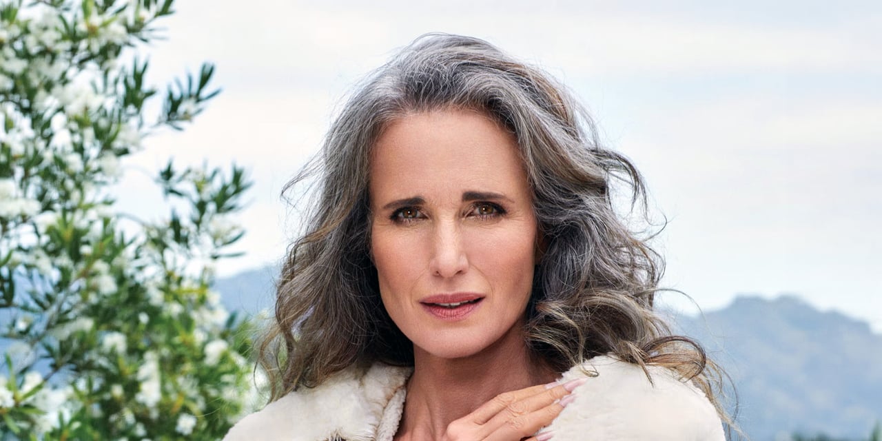 Woman with long, wavy salt-and-pepper hair in loose layers past the shoulders, parted in the middle