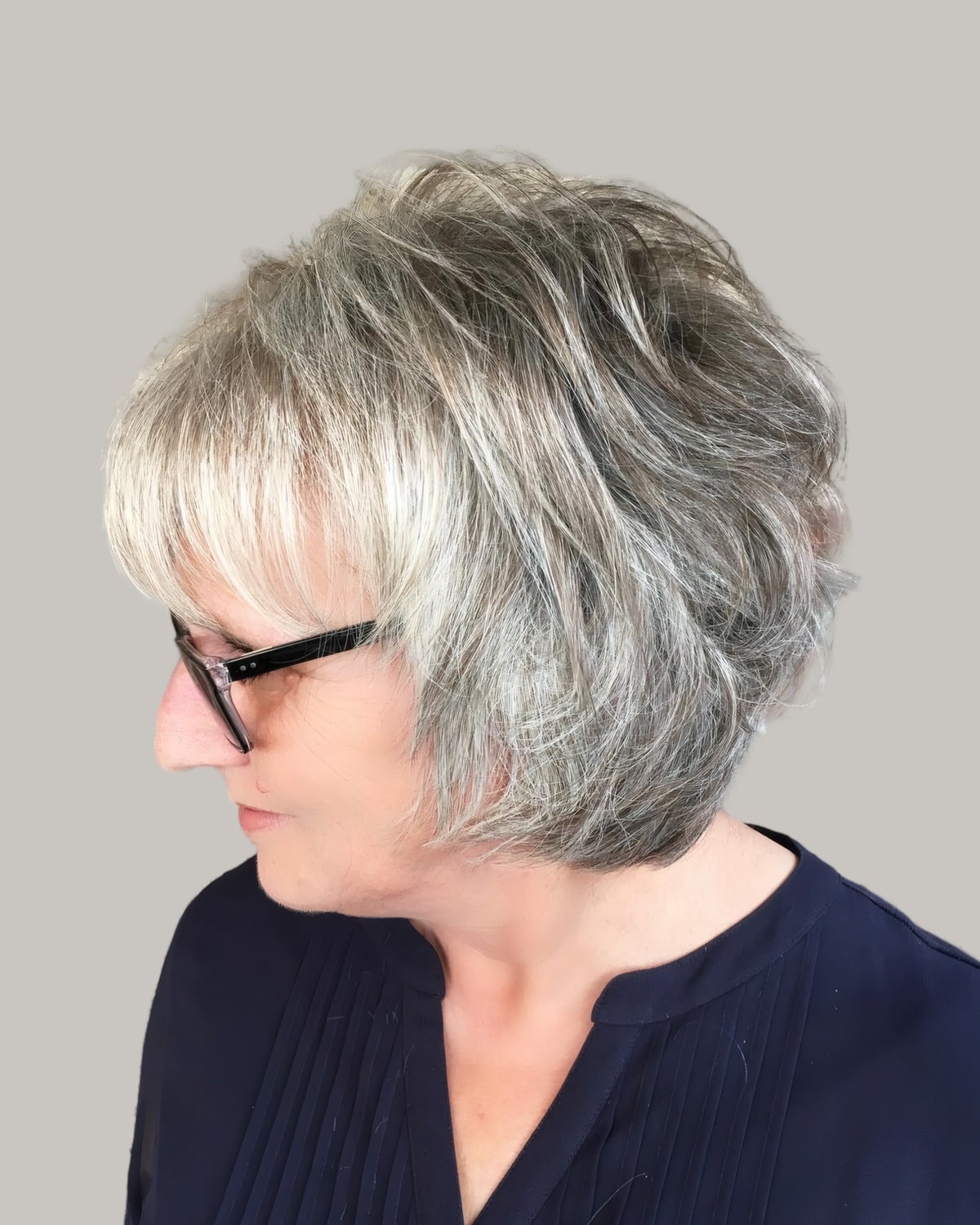 Woman with a gray shag, a fringe and dark glasses, looking down