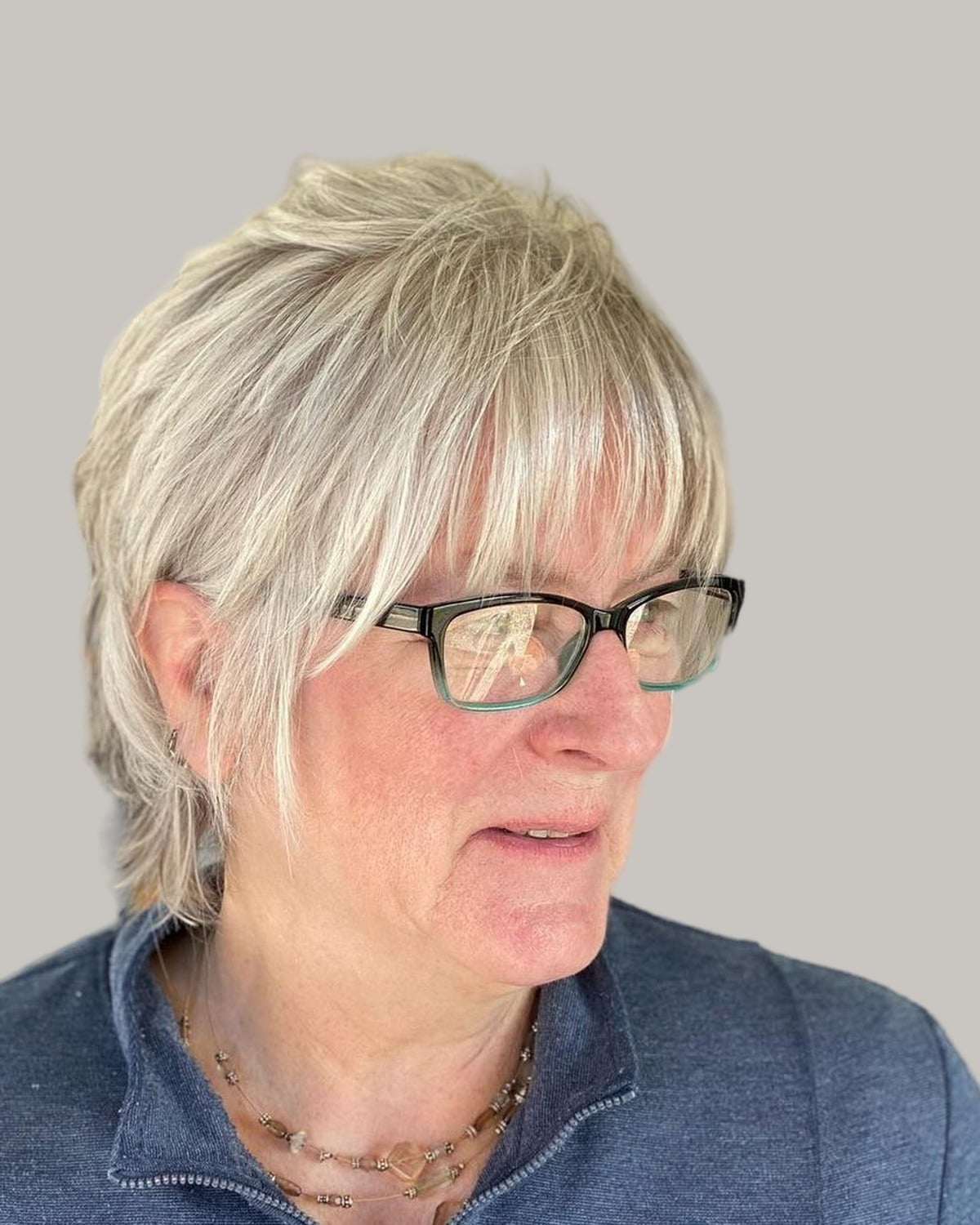 Woman with a blonde-gray shag, a fringe and black glasses