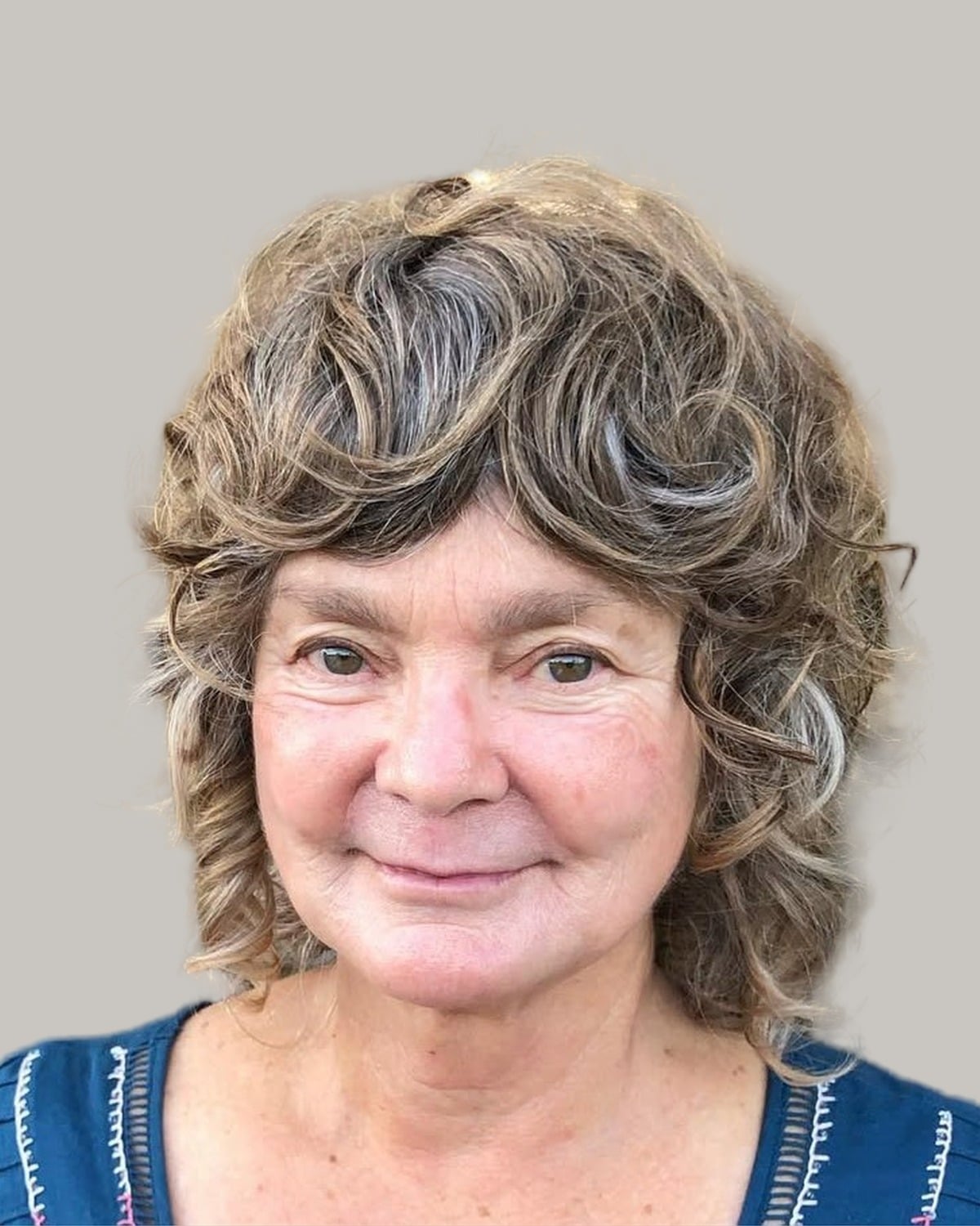 Smiling woman with a curly gray shag and a full curly fringe