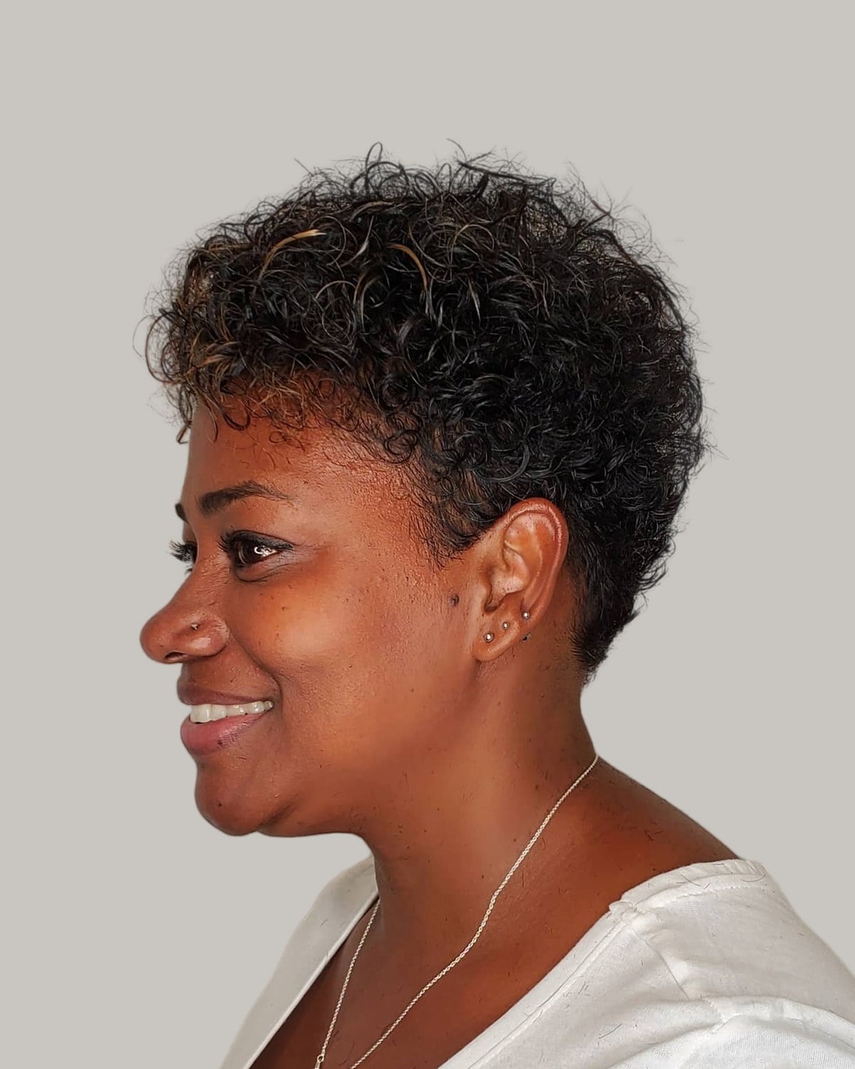 Smiling woman with a short, coily pixie, seen in profile
