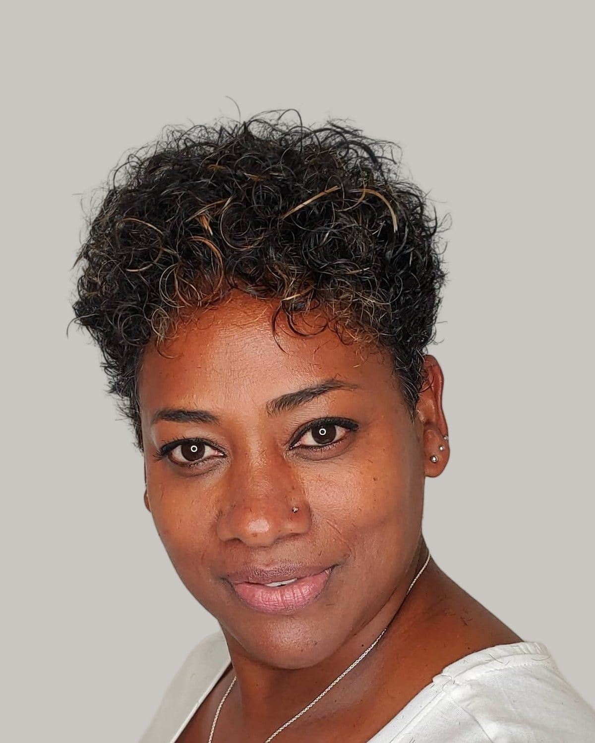 Smiling woman with a short, coily pixie and a round face, in a white top
