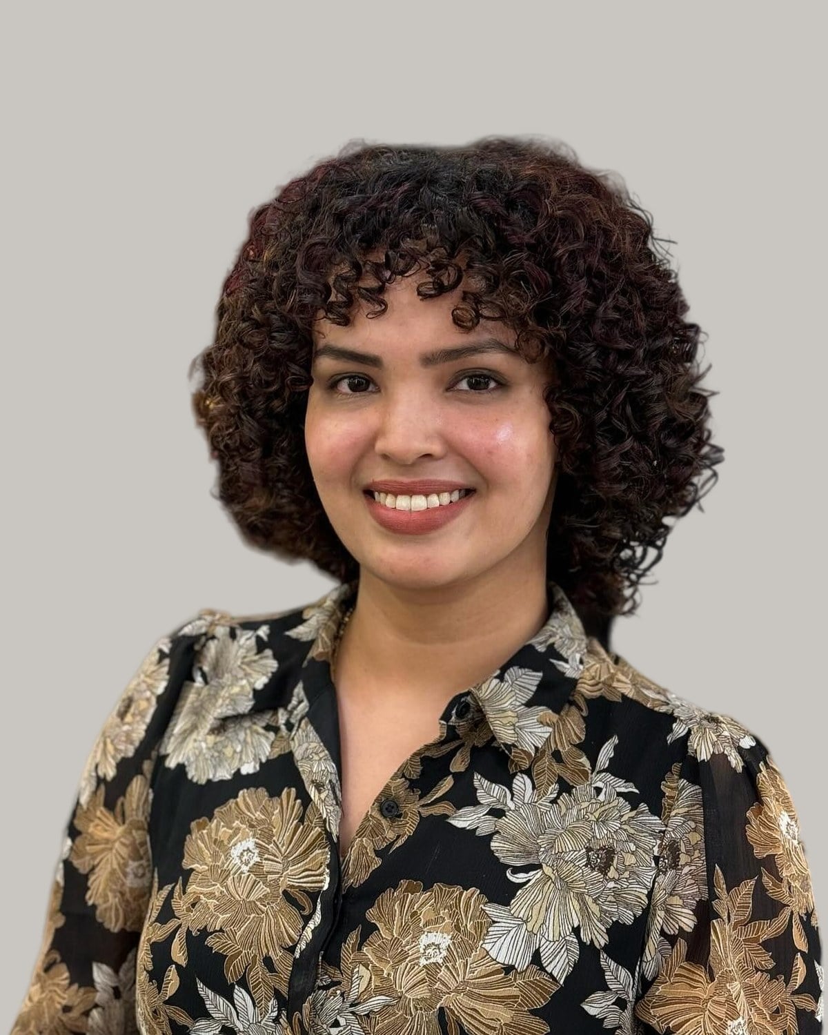 Smiling woman with a short, dark-brown curly bob, in a floral blouse